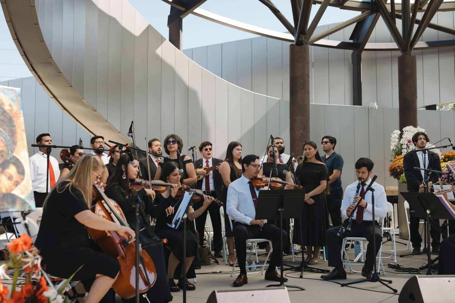 Musicians performing in an ensemble under architectural beams in a bright space.