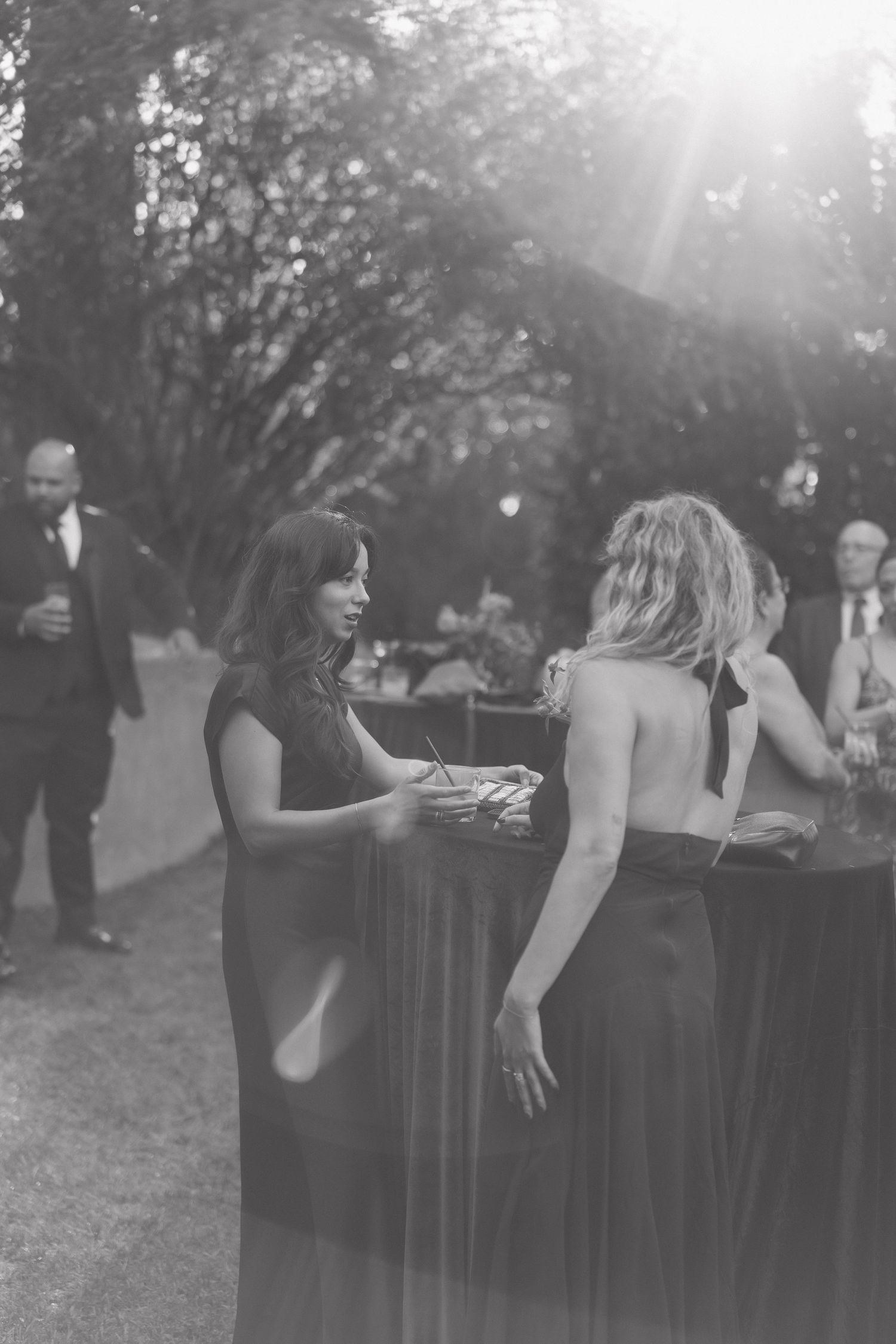 Black and white photo of wedding guests mingling at an outdoor reception.