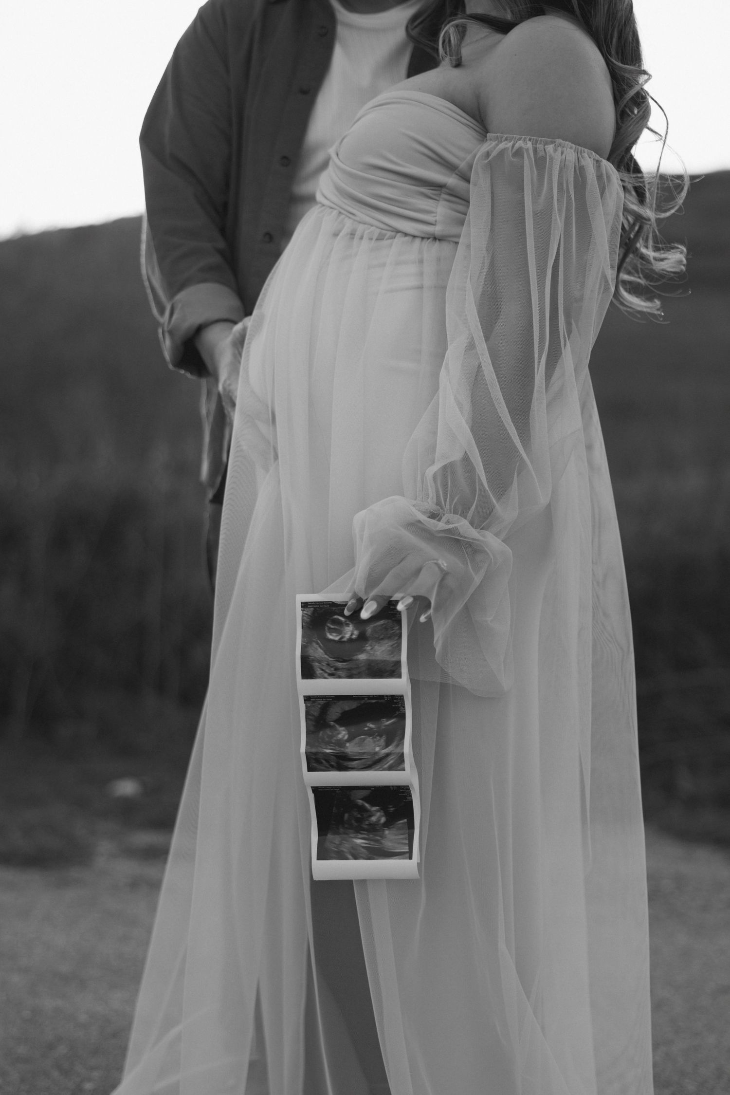 Black and white maternity photos showing sonogram images held against flowing dress.