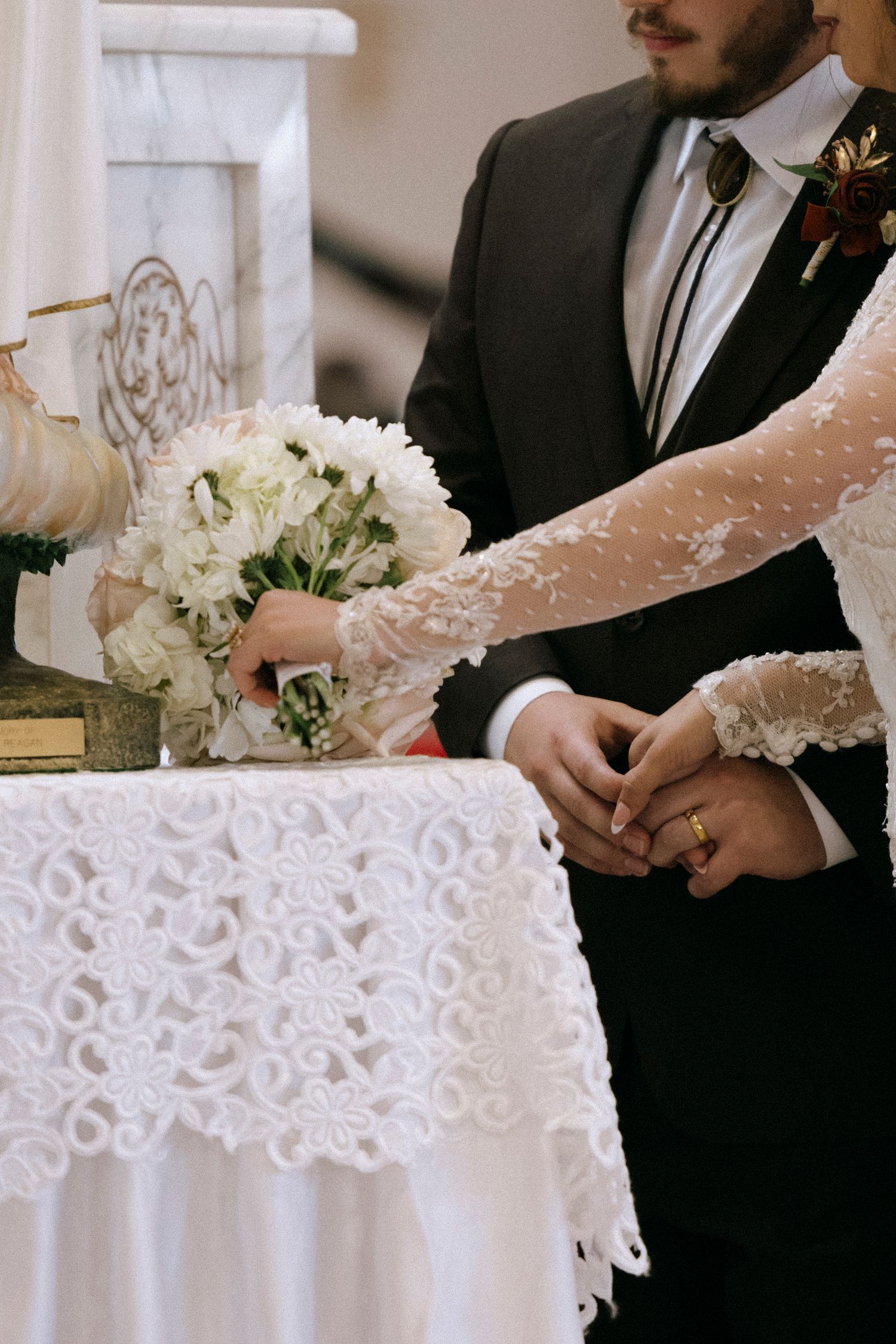 Close-up details of a bride's lace wedding dress and bouquet during the ceremony.