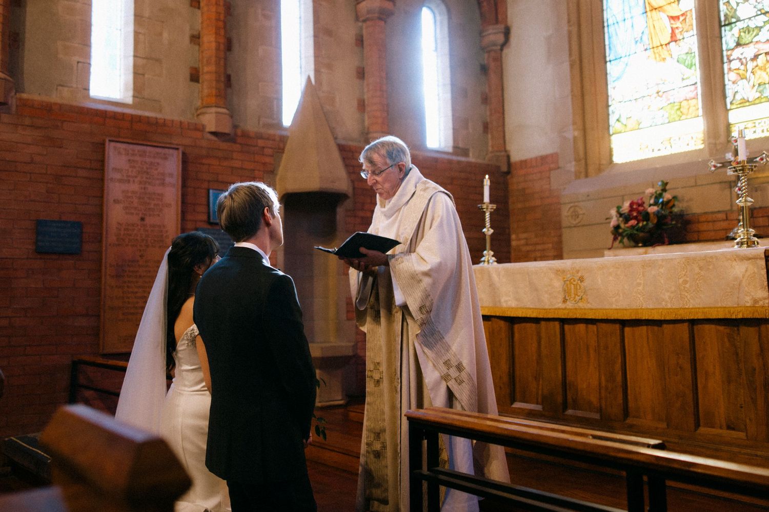 Sunlit church interior with stained glass windows during wedding ceremony.