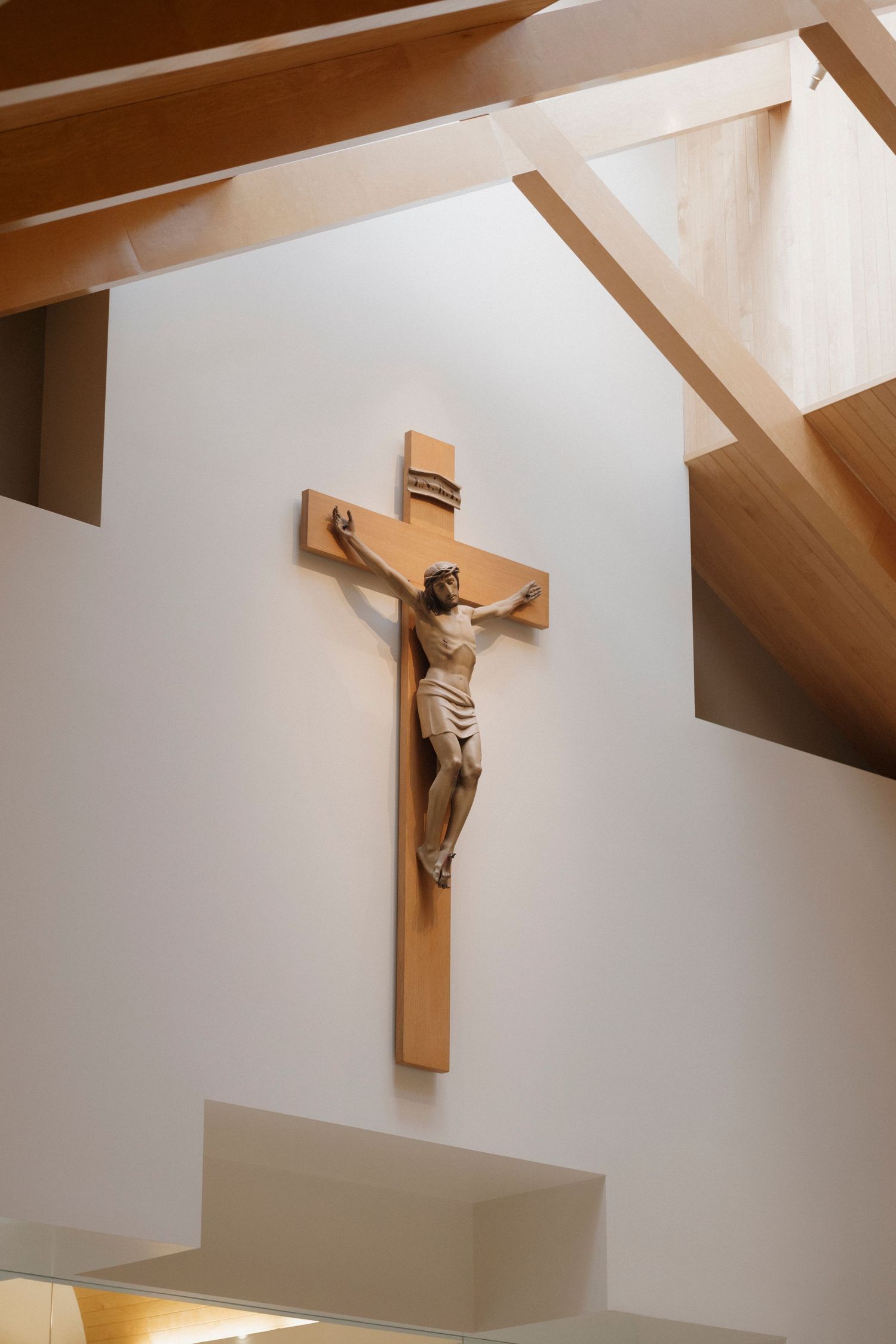 Wooden crucifix mounted on white wall in modern church interior.