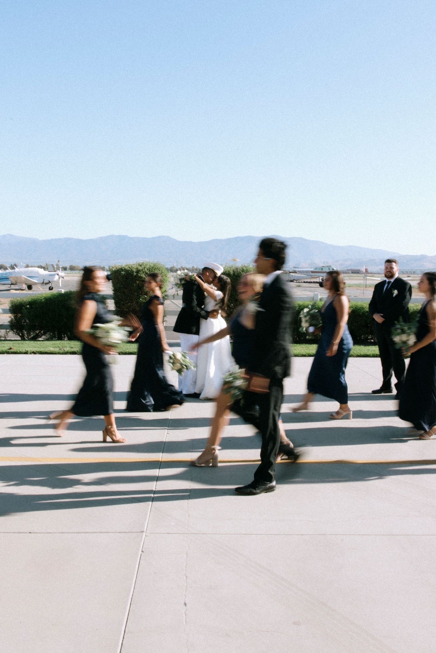 Motion blur of wedding party running across outdoor venue with mountains in background.
