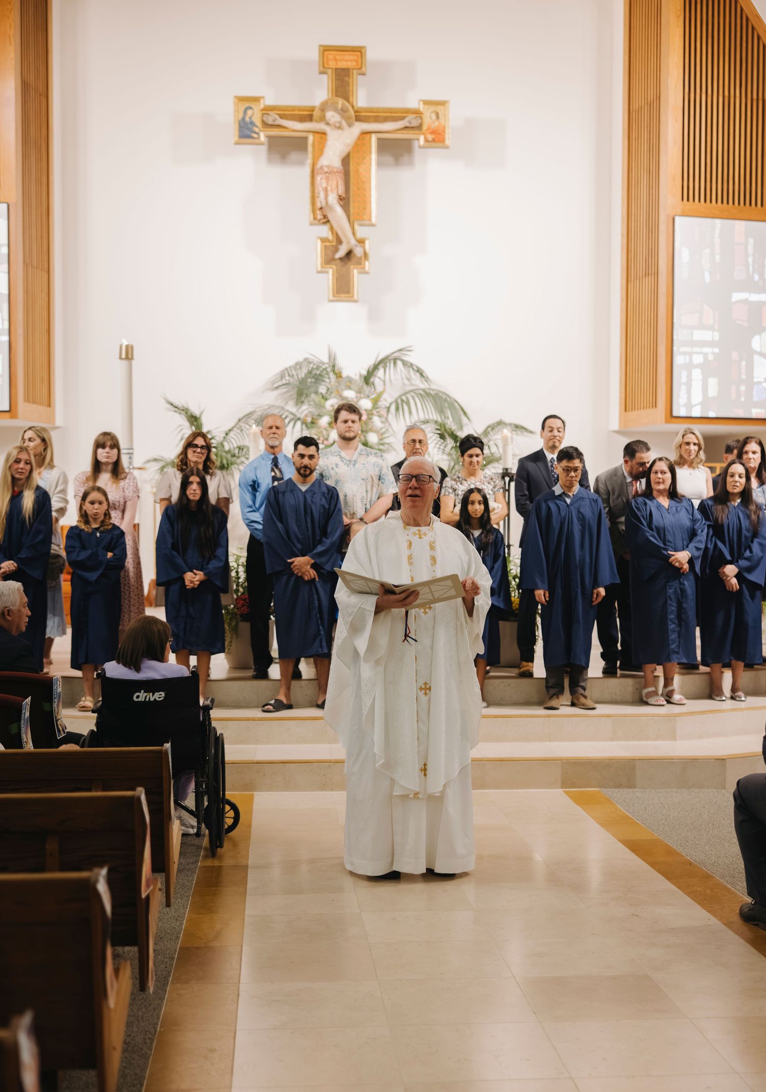 Catholic priest leading RCIA candidates in blue robes before crucifix during Easter Vigil Mass.