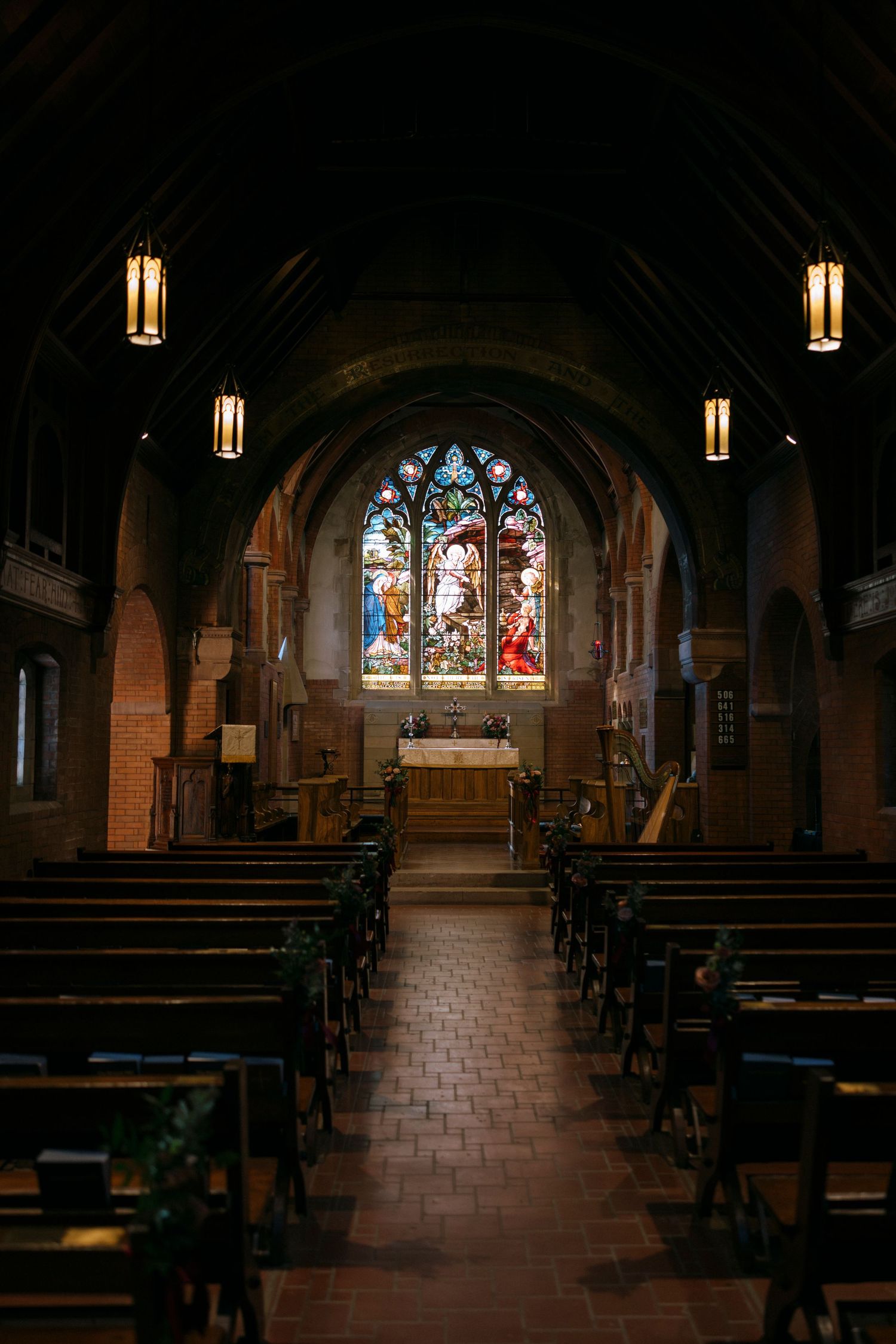 Dark interior of church sanctuary with stained glass windows and wooden pews leading to altar.