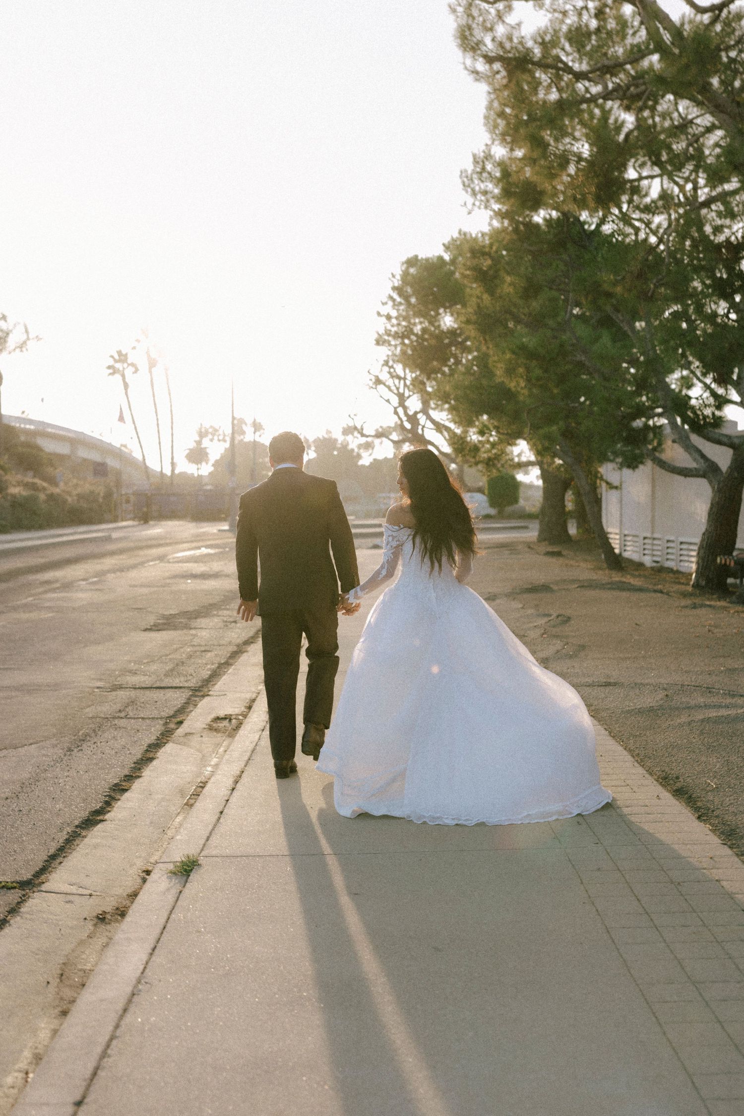 Wedding couple walking along a sunlit path casting long shadows.