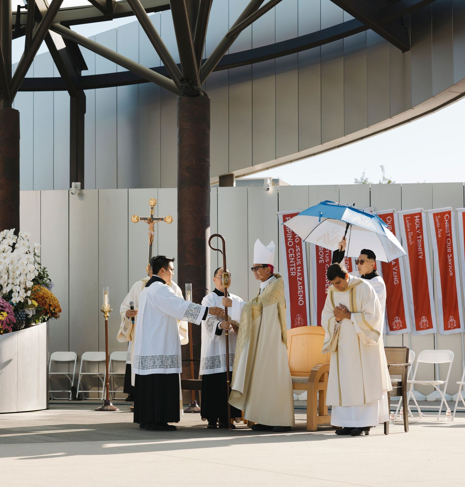 Indoor religious ceremony space with white-robed clergy and folding chairs arranged in rows.