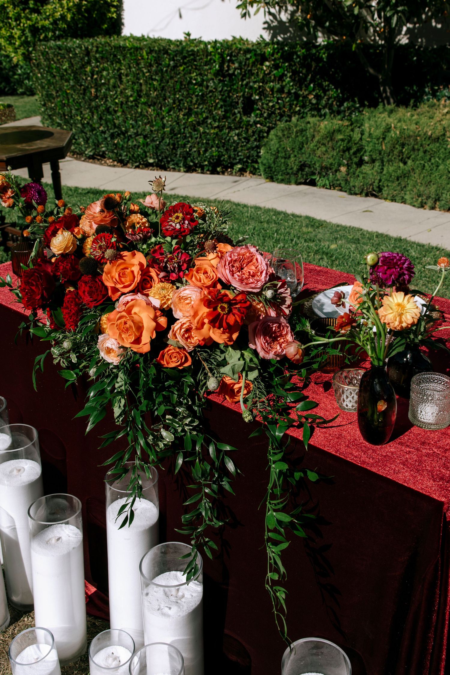 Elegant floral centerpieces with coral and burgundy roses arranged in white vases on a dark tablecloth.