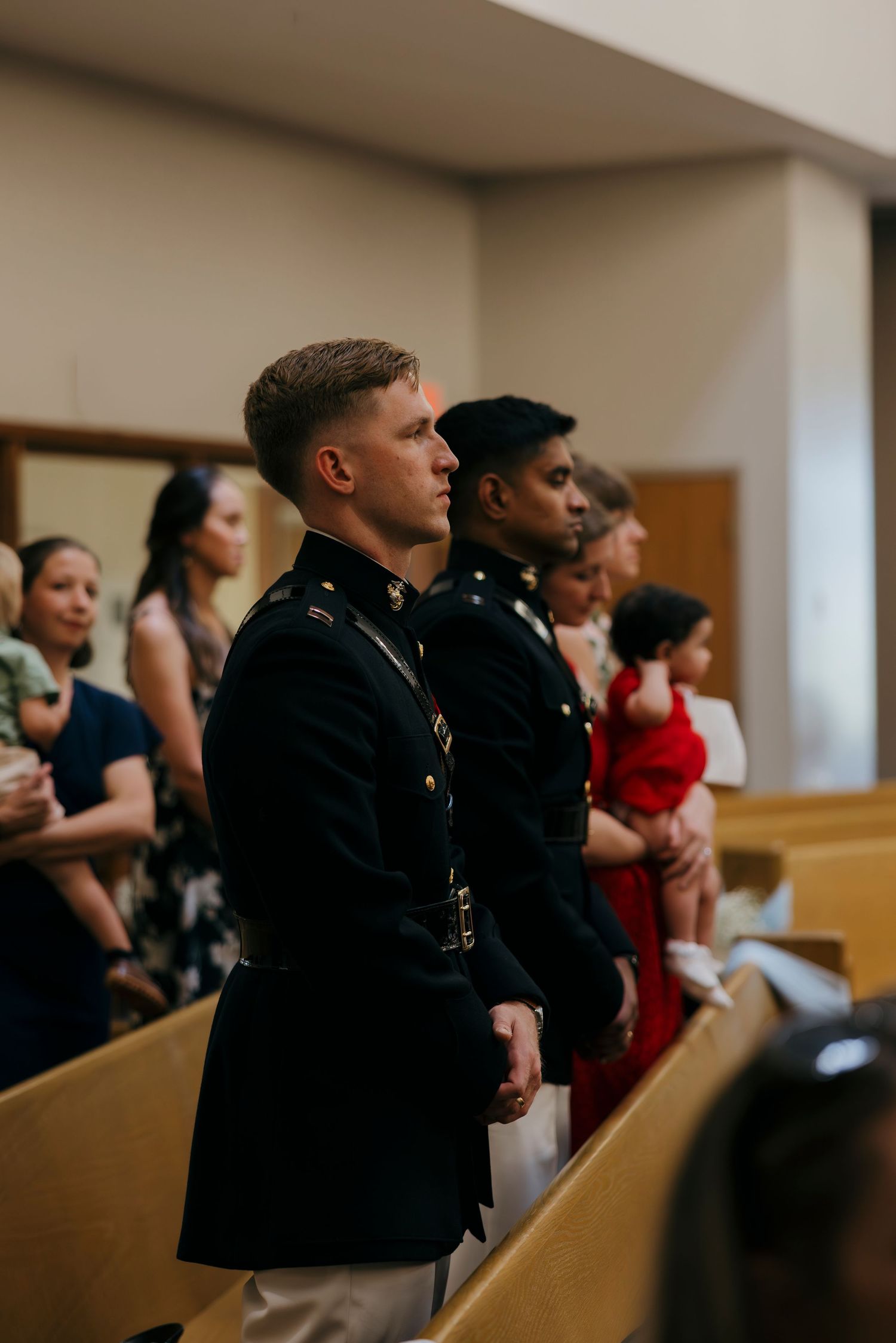 Two military officers in dress uniforms stand attentively in church pews during a formal ceremony.