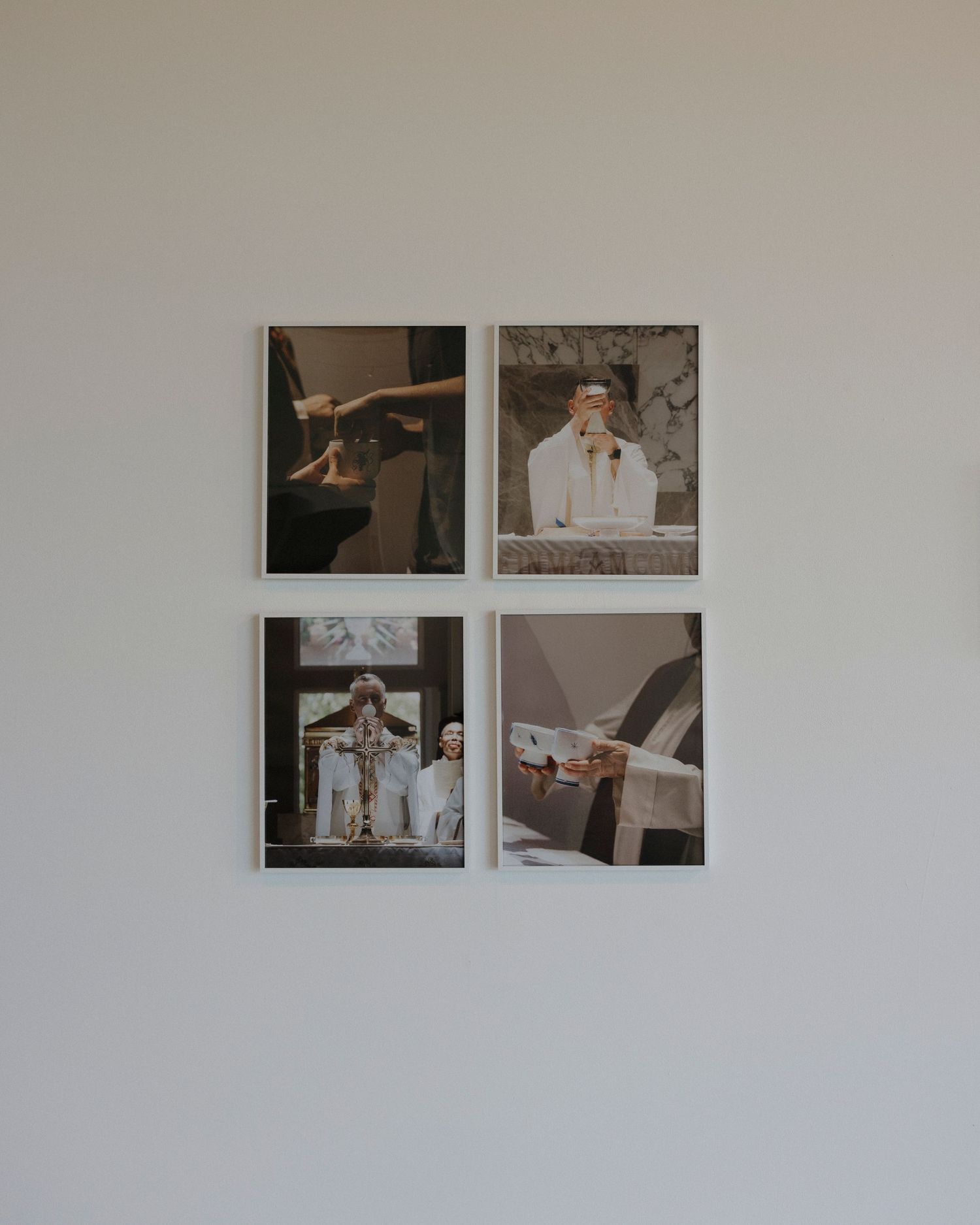 Small black and white photographs arranged in pairs on a clean white gallery wall.