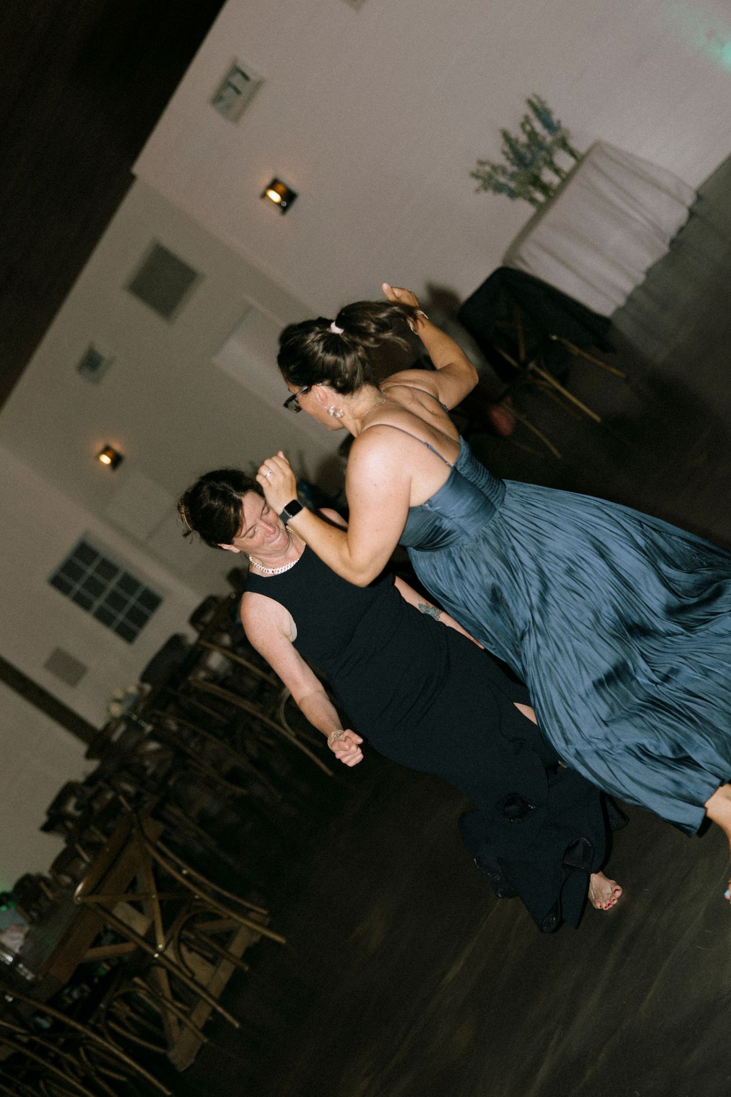 Two people dancing elegantly at a formal event, wearing black and blue gowns in a softly lit venue.