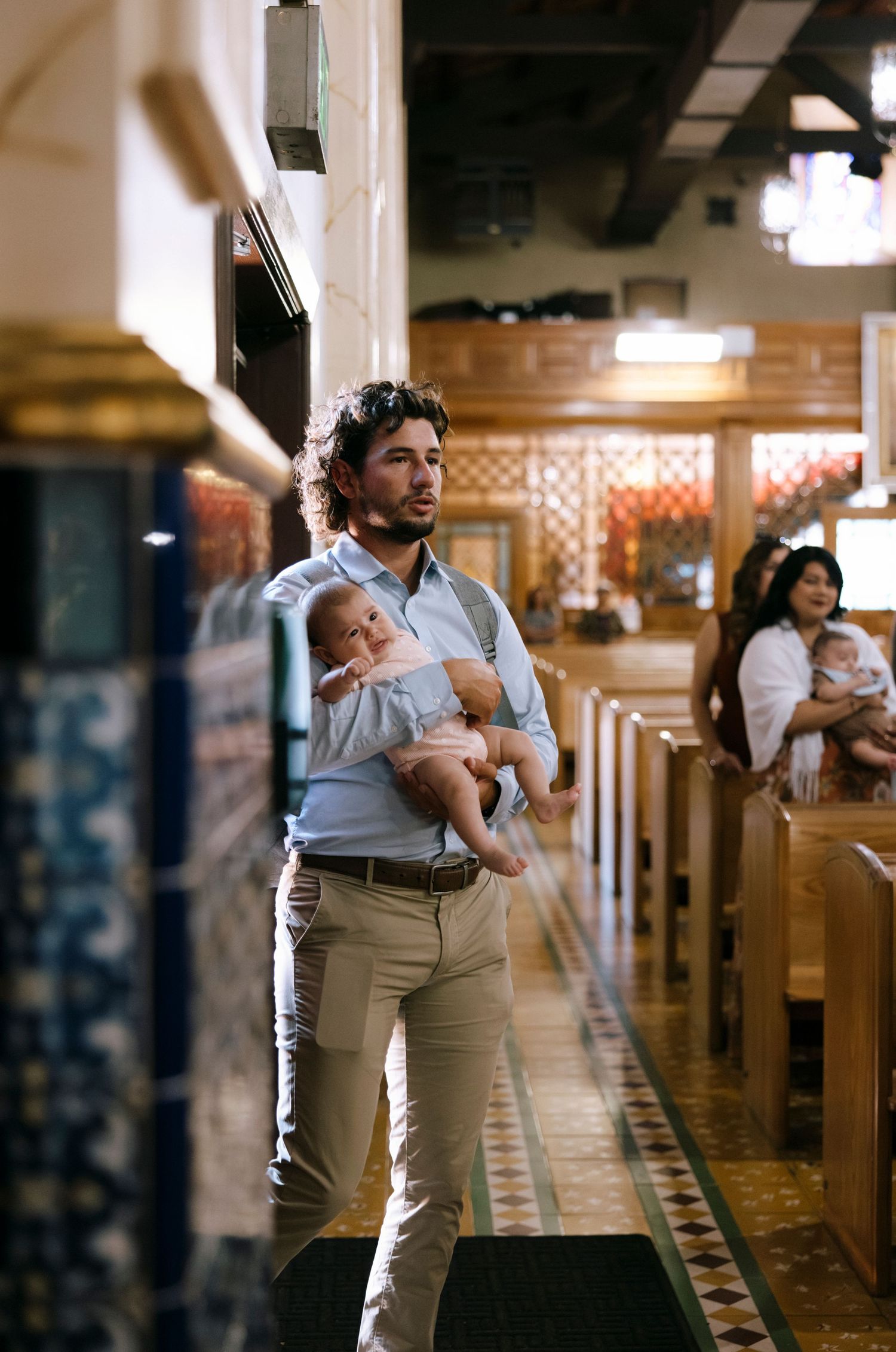 A parent holds a sleeping baby while standing in a church aisle during a ceremony.