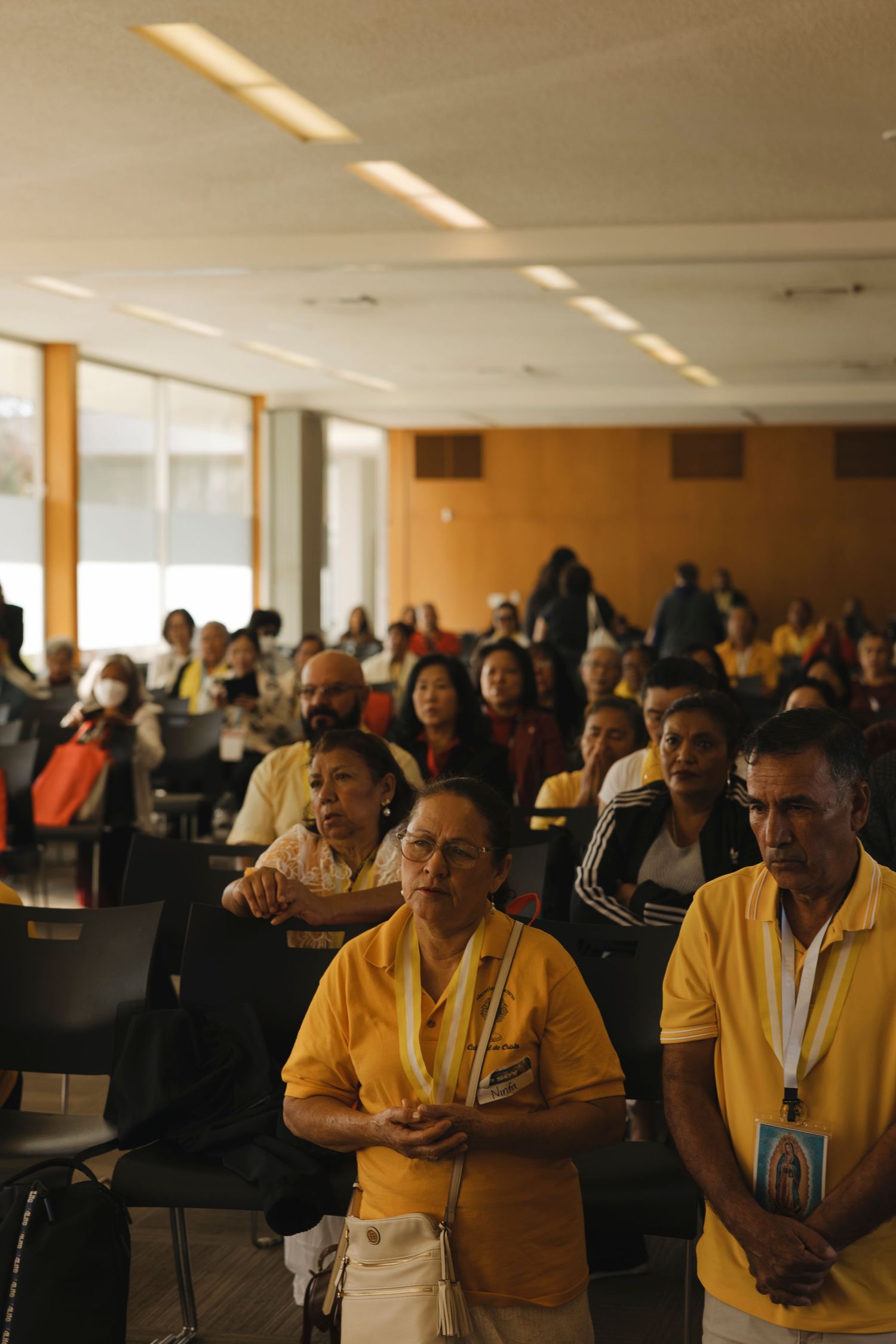 Attendees in yellow shirts listening intently at an indoor conference.