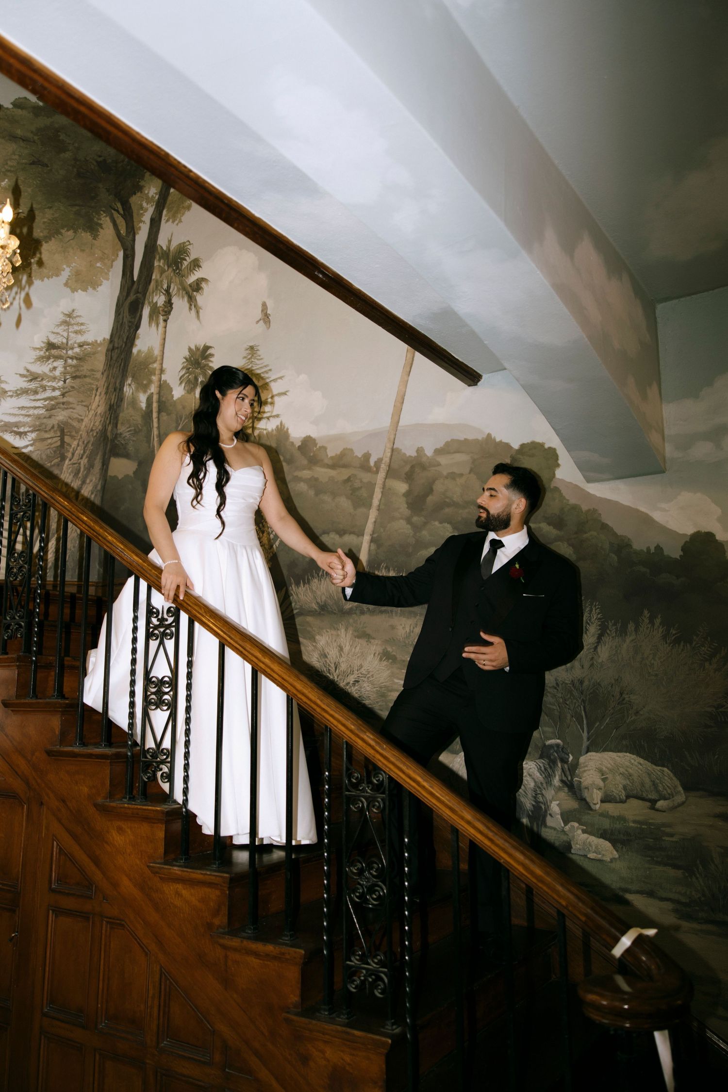 Artistic wedding photos captured on ornate staircase with landscape mural background.