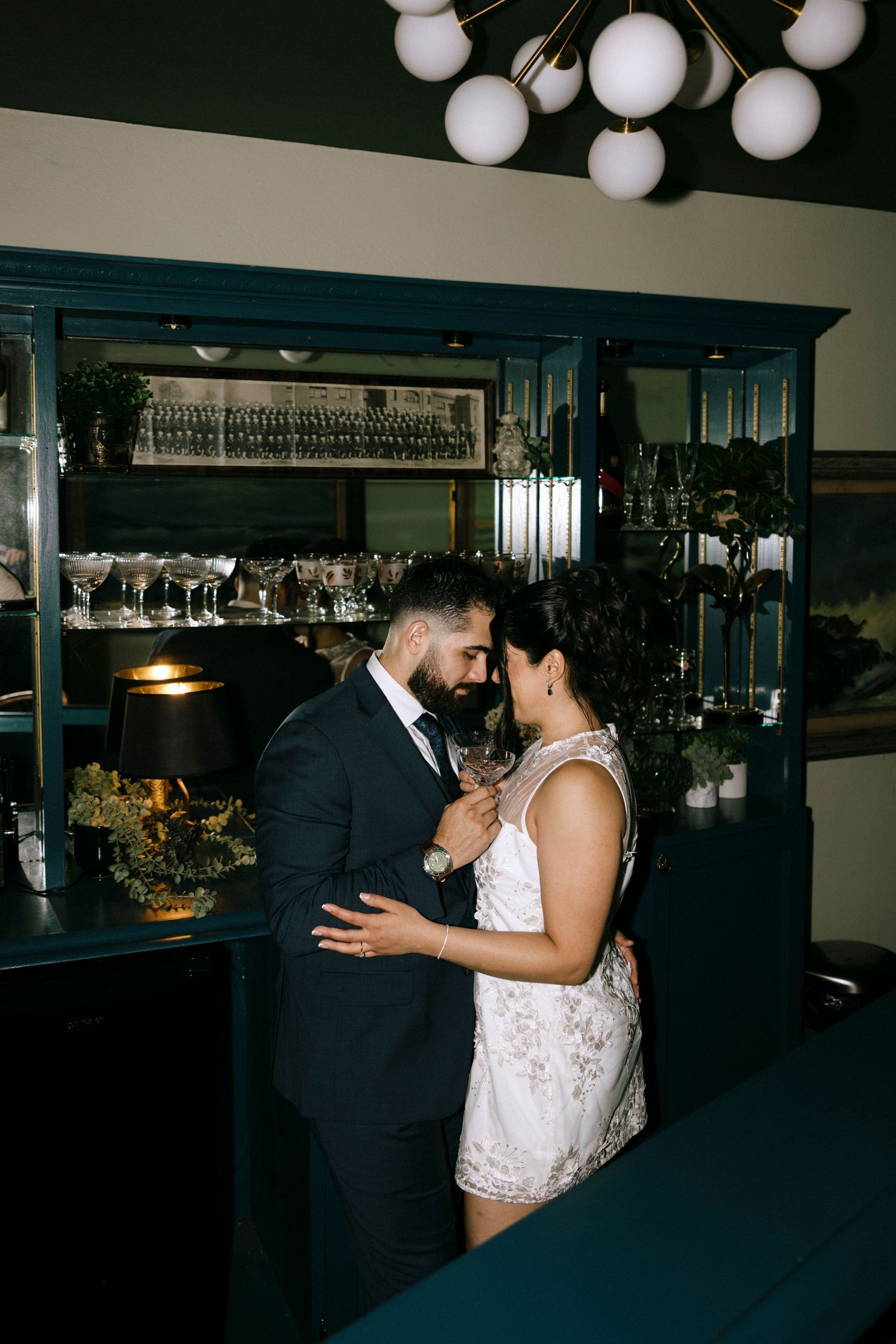Wedding couple dancing and laughing together under decorative lighting at indoor reception.