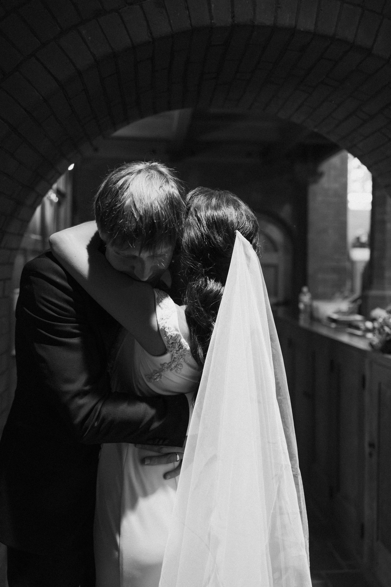 Artistic black and white shot of wedding couple dancing in arched hallway.