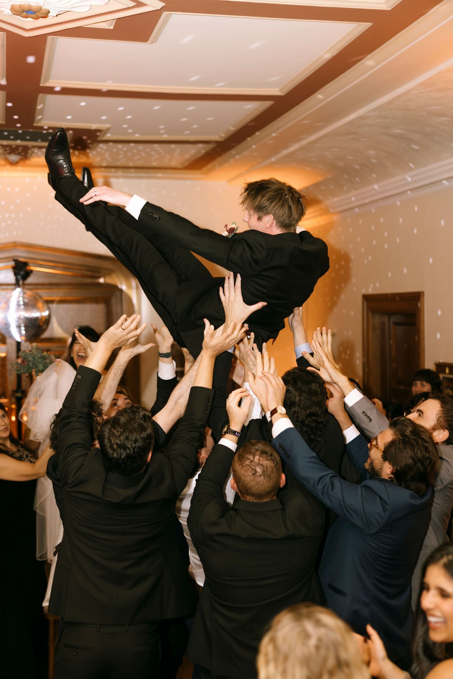 Group of party guests dancing with hands up under sparkling lights at a celebration.