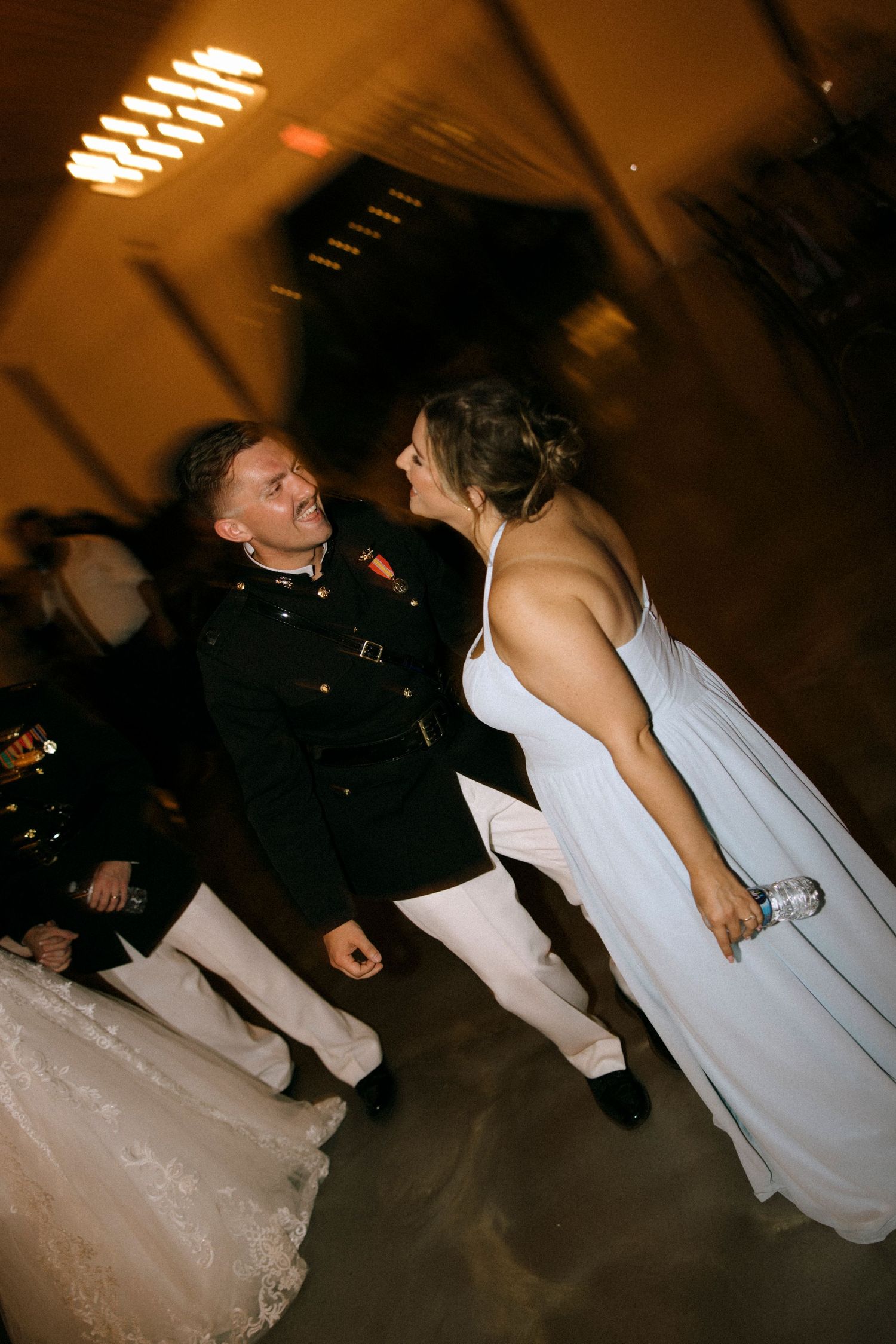 Military groom in dress uniform shares joyful dance with bride in white gown at elegant wedding reception.