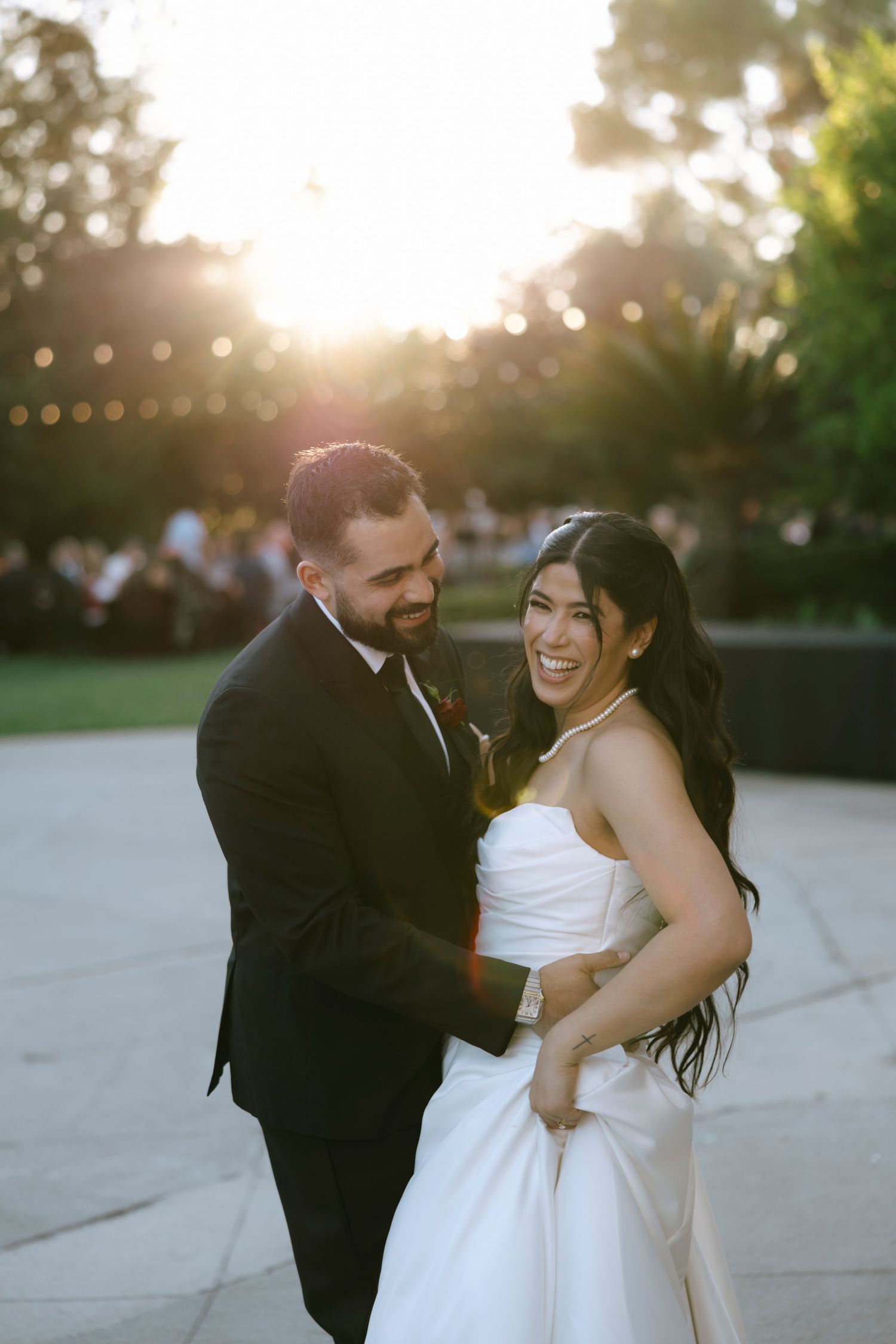 A couple shares a joyful moment at sunset with string lights glowing in the background.