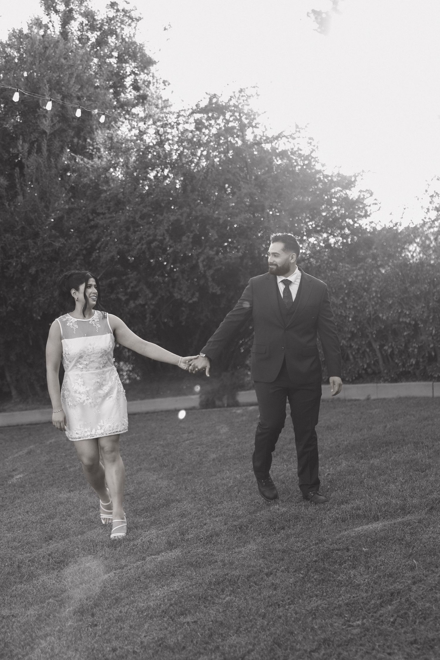 Black and white photo of couple walking playfully across grassy hillside.