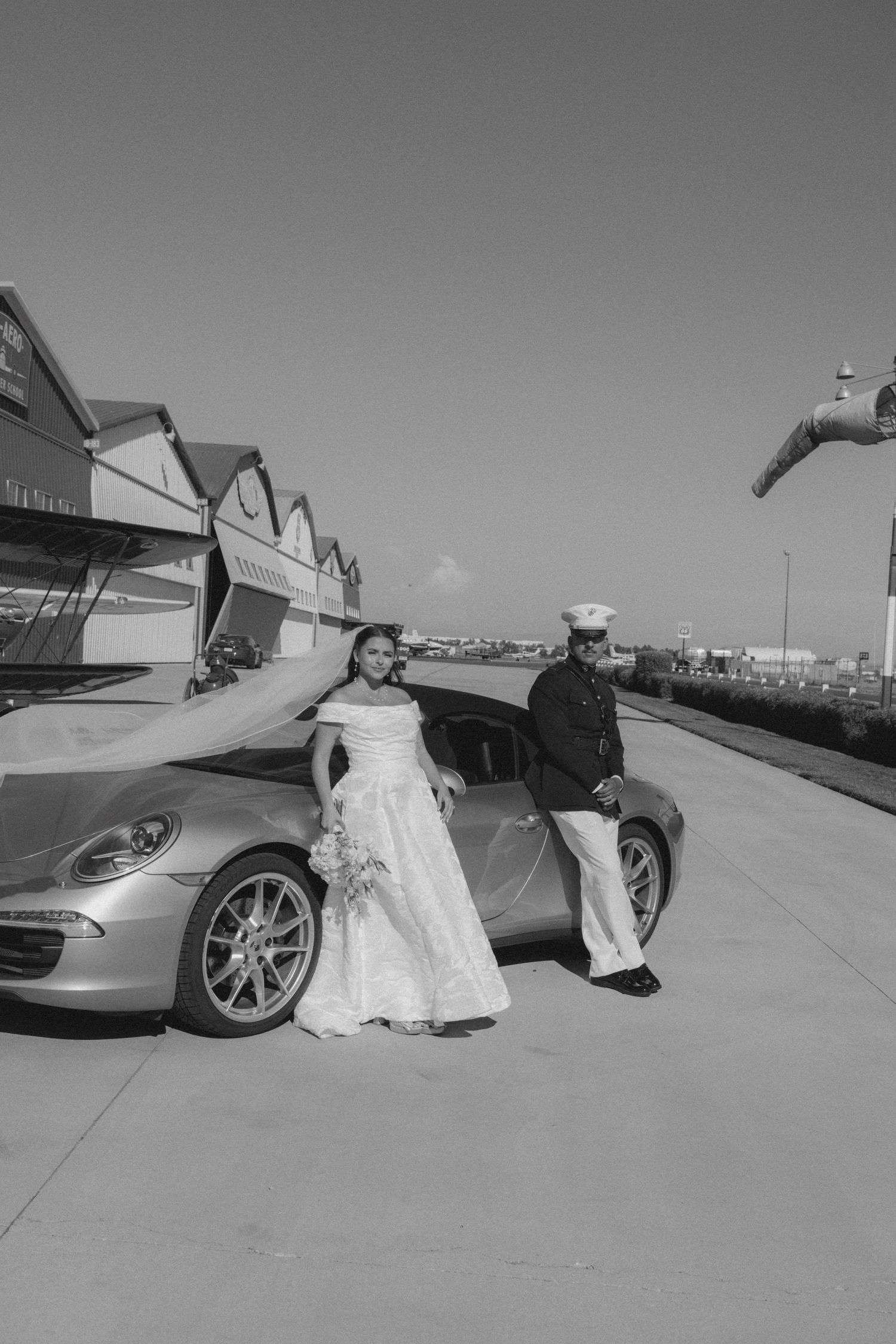 Black and white wedding photo with luxury sports cars in the background.