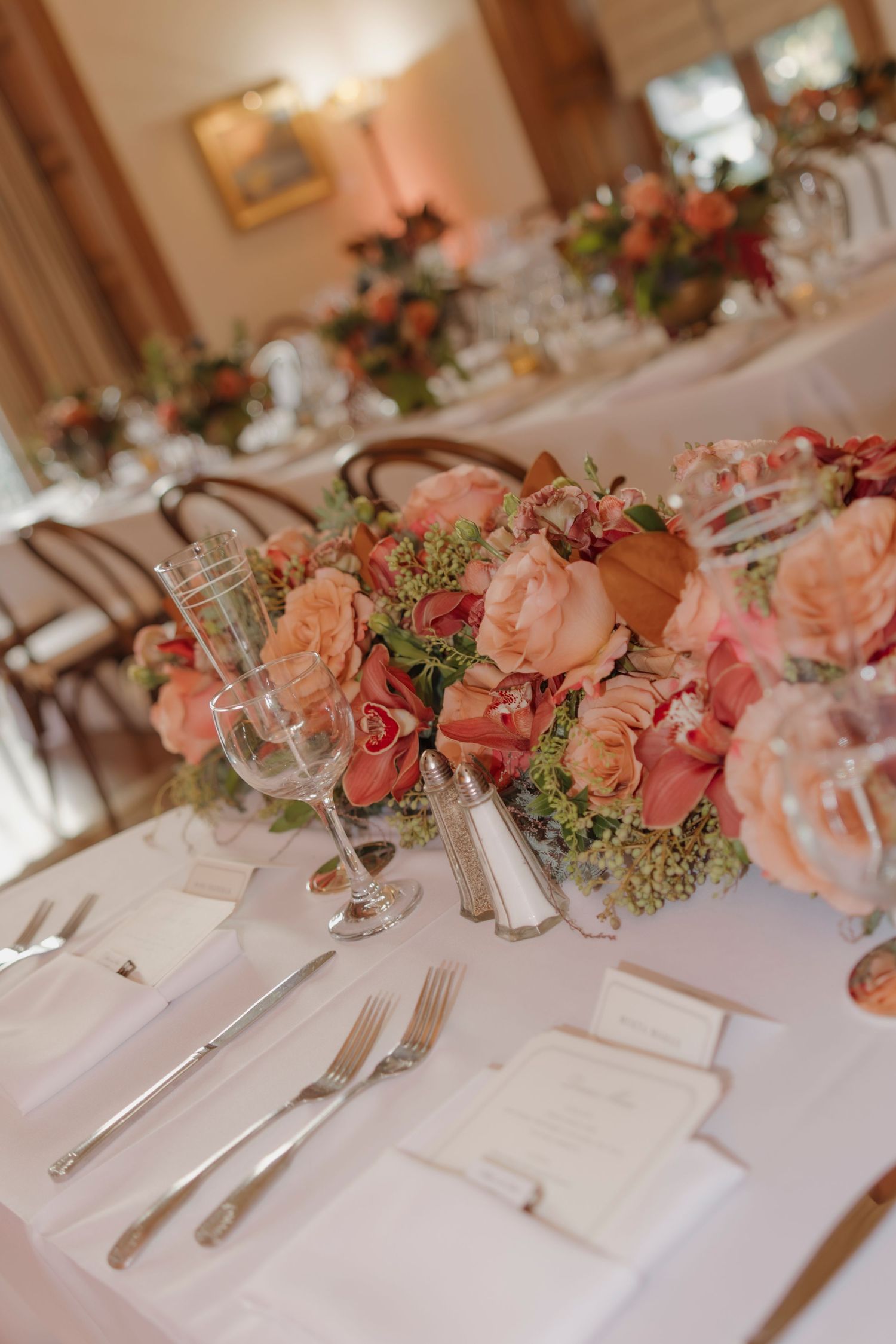 Long dining table decorated with pink and coral floral arrangements and crisp white table settings.
