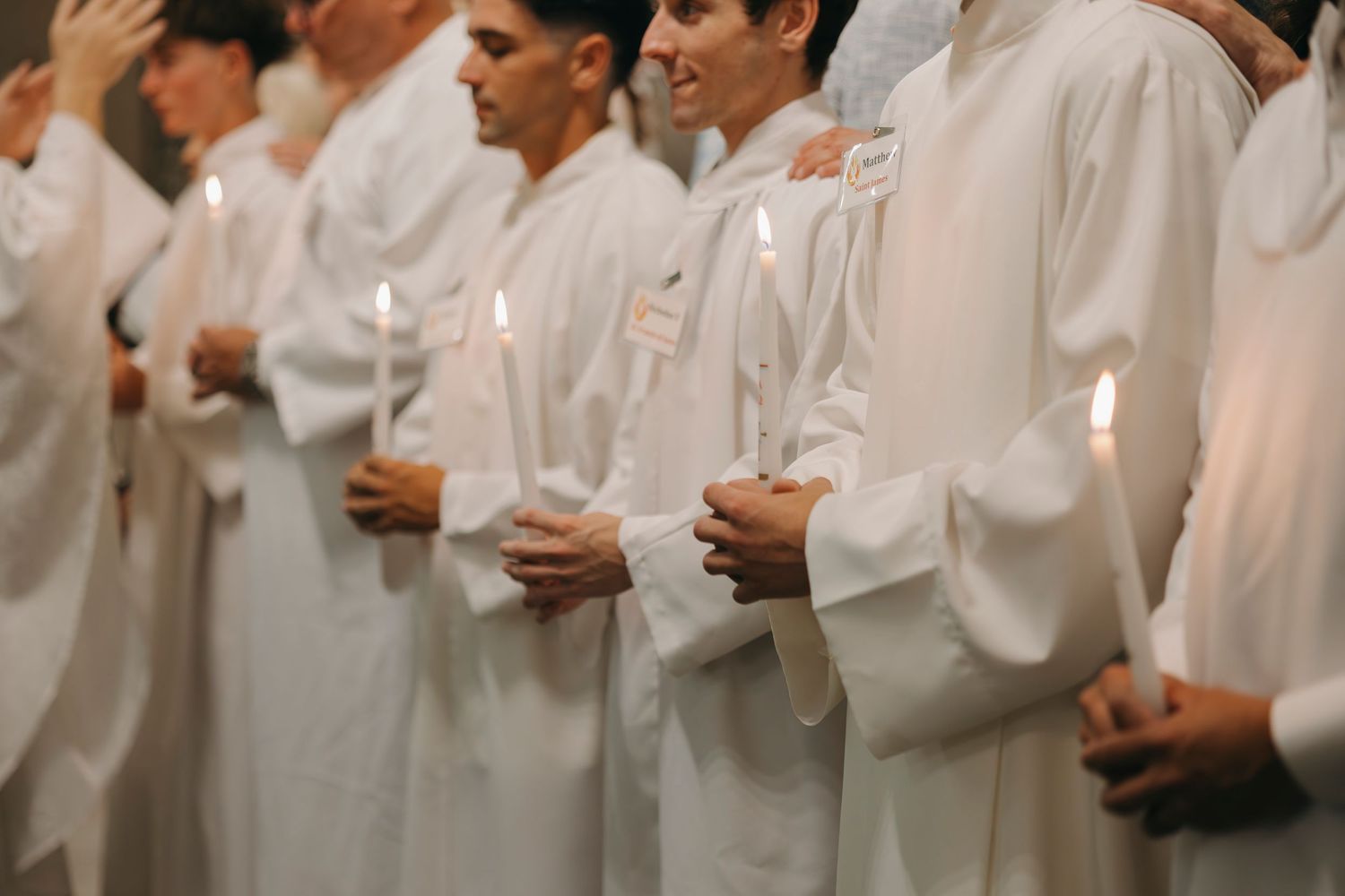 Newly baptized Catholic converts in white albs holding candles during Easter Vigil Mass.