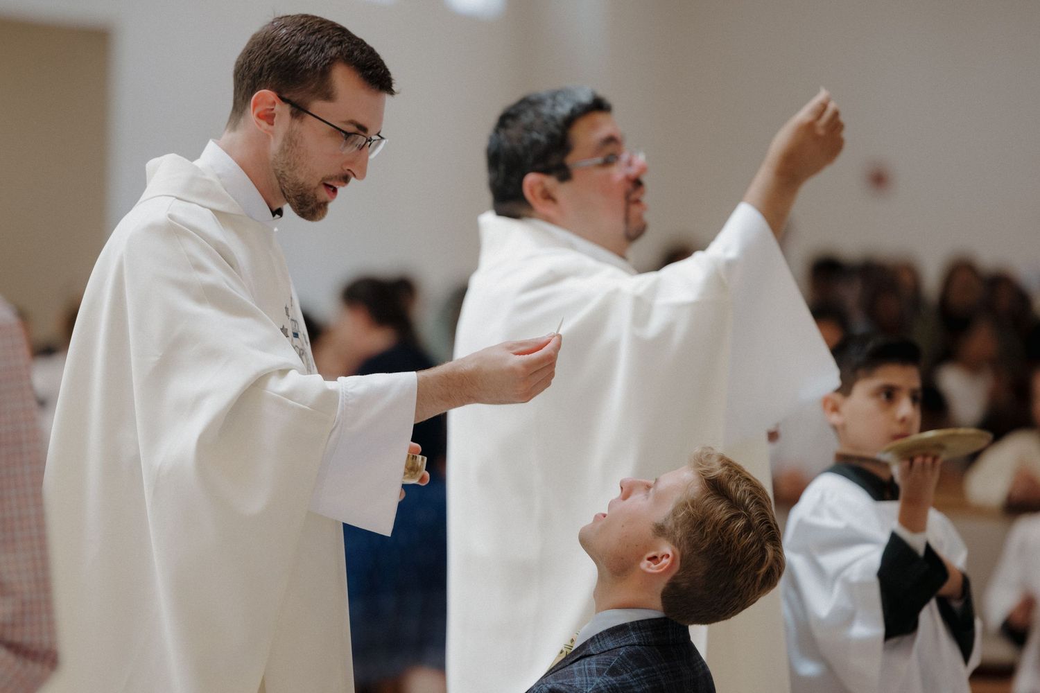 A priest in white robes distributes communion during a religious ceremony.