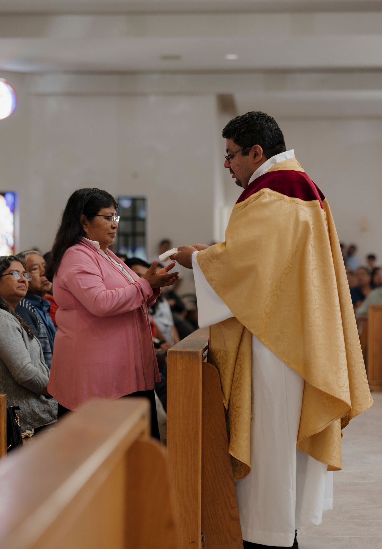 People standing in church pews with golden cloth draped over the ends during a religious service.