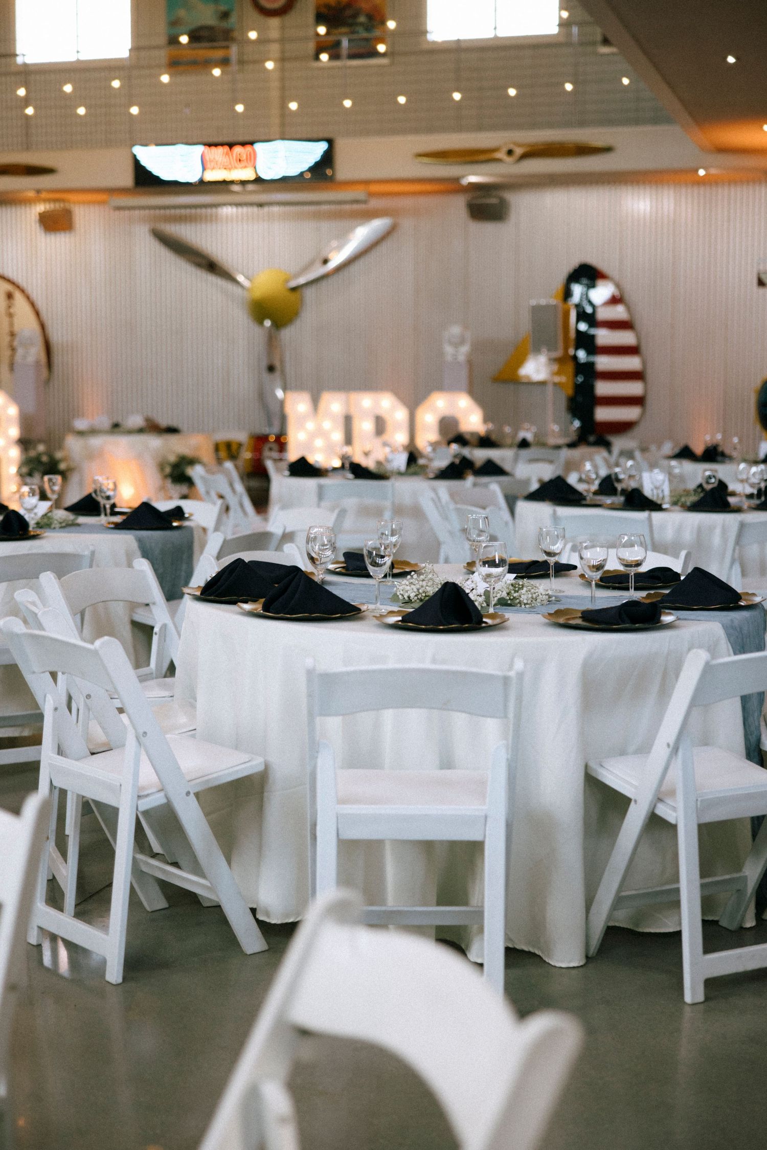 Elegant reception venue with white folding chairs and round tables set for a wedding celebration.