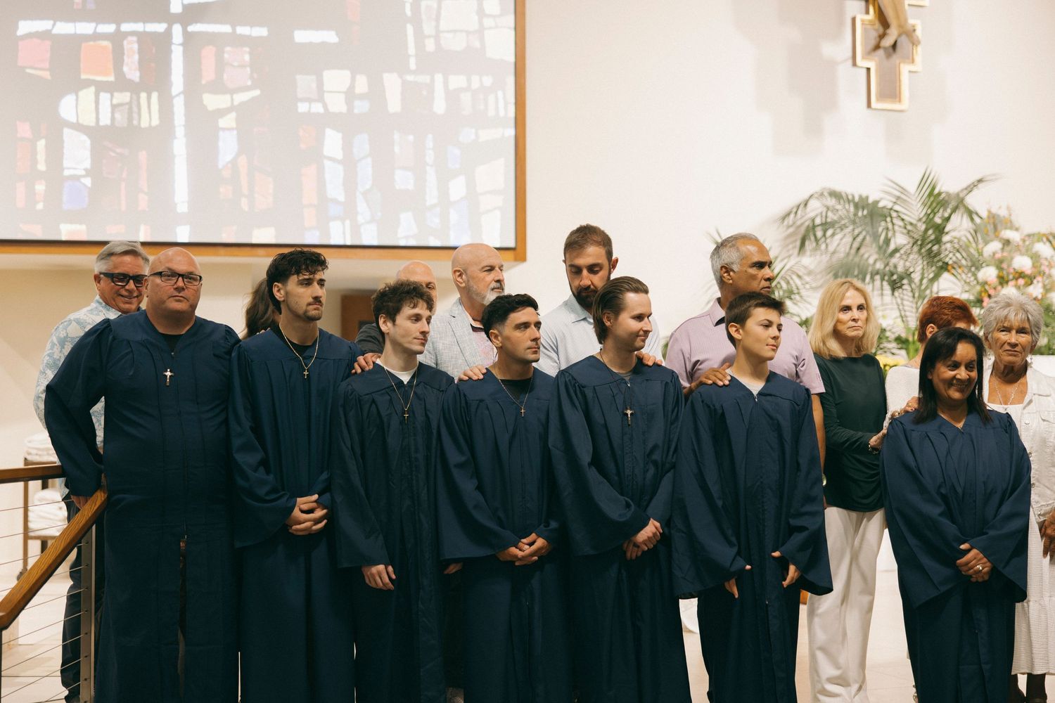 Group of students in blue graduation gowns posing with adults in a church ceremony setting.