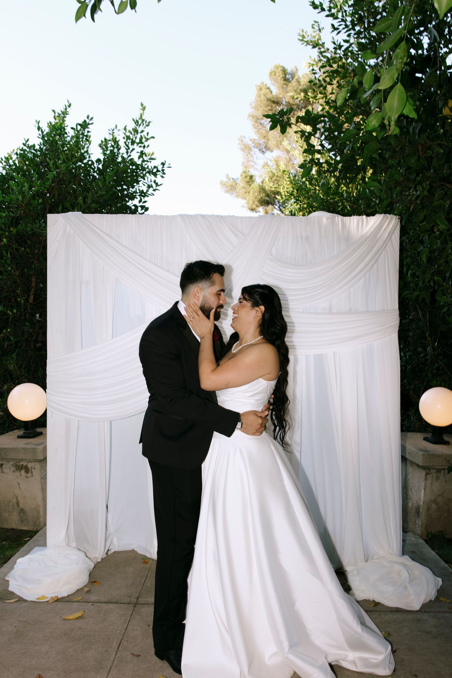 A couple shares an intimate moment against a white draped backdrop at their wedding.
