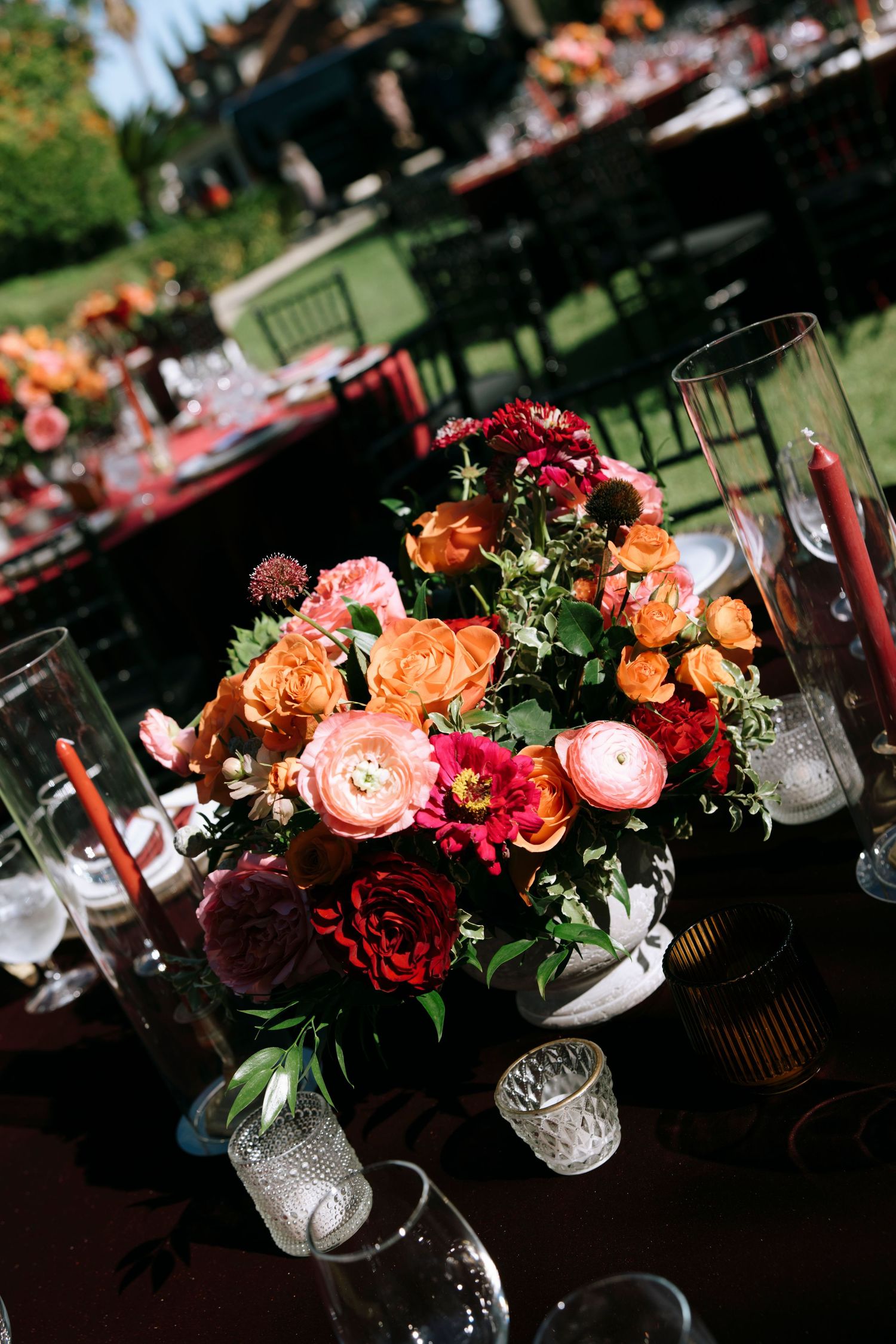 Romantic table settings with colorful rose arrangements in white vases against an outdoor backdrop.