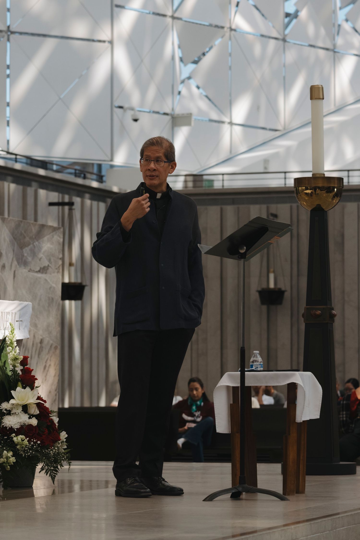 Speaker in black attire presenting from a podium in a bright modern space.