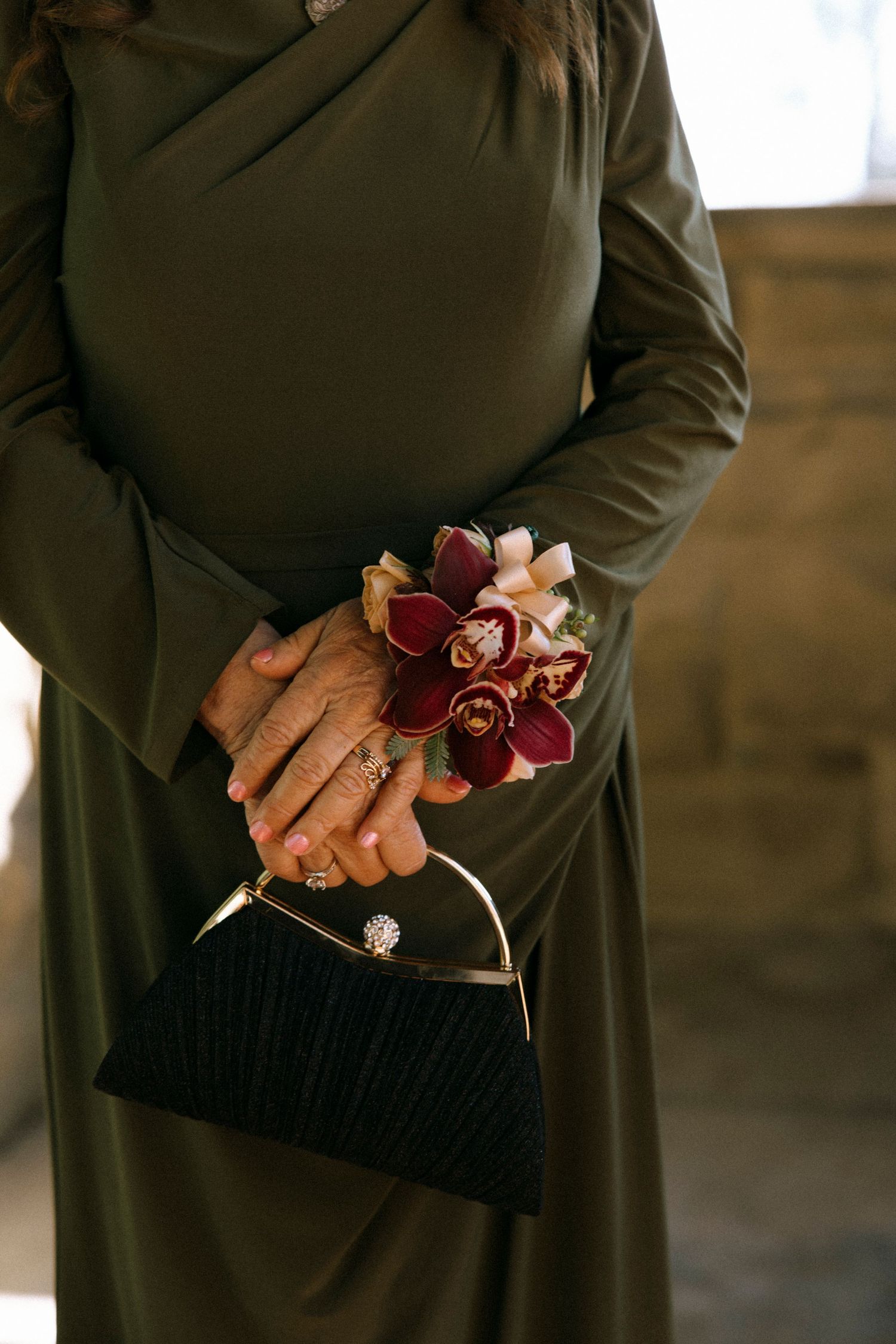 Close-up of hands holding delicate pink and burgundy floral corsage against dark formal attire.