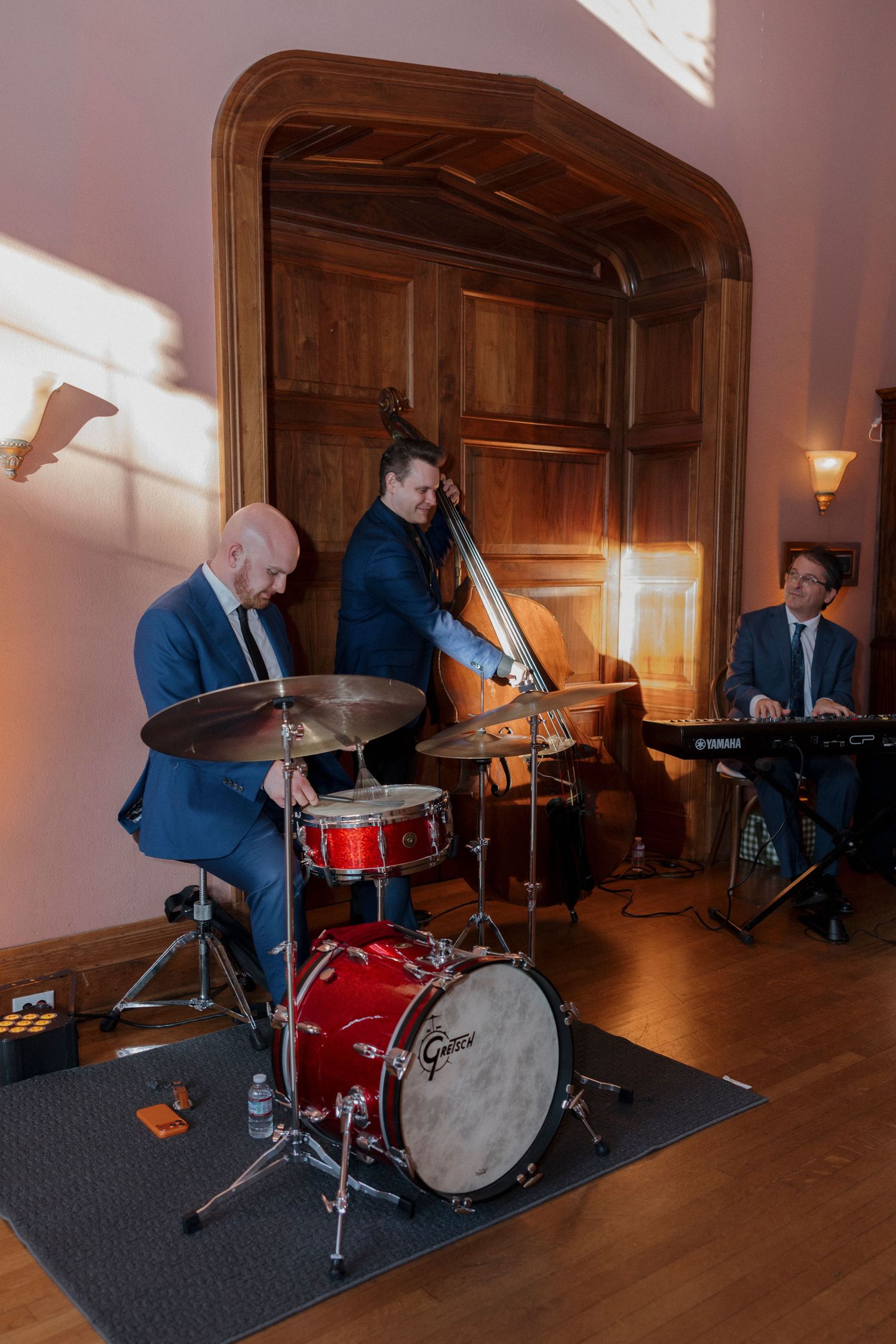 Musicians setting up drum kit and instruments in an elegant wood-paneled room.