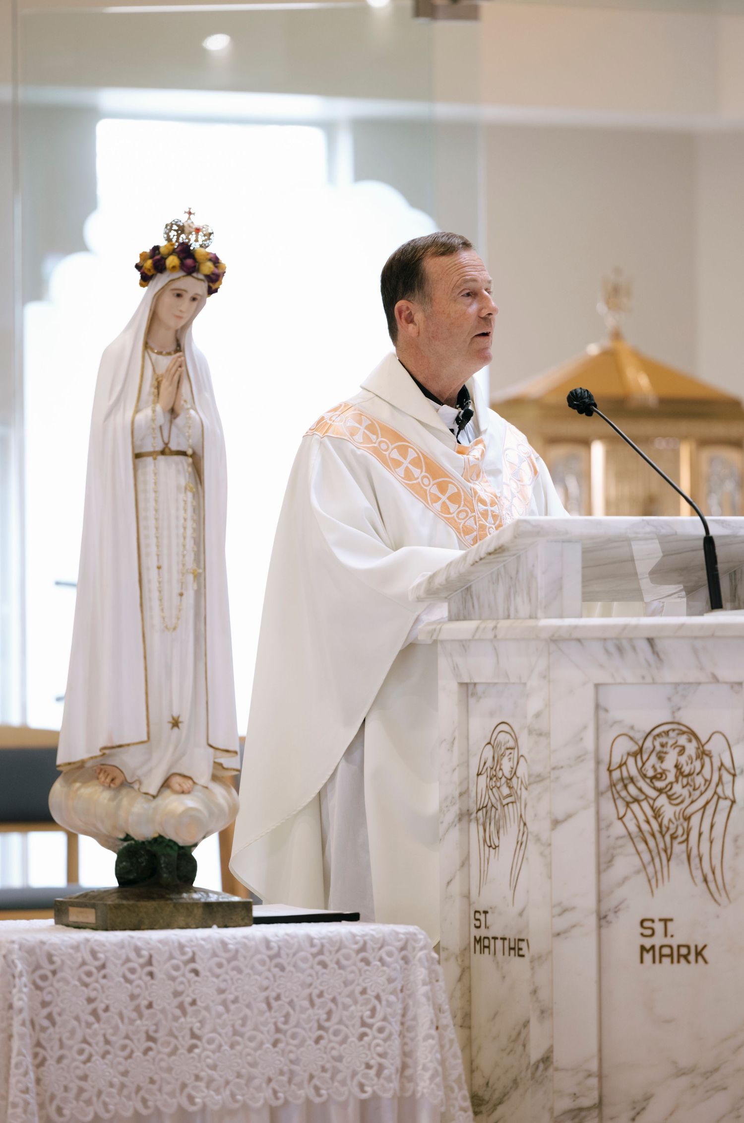 Priest in white robes conducting ceremony at decorated marble altar in Catholic church.
