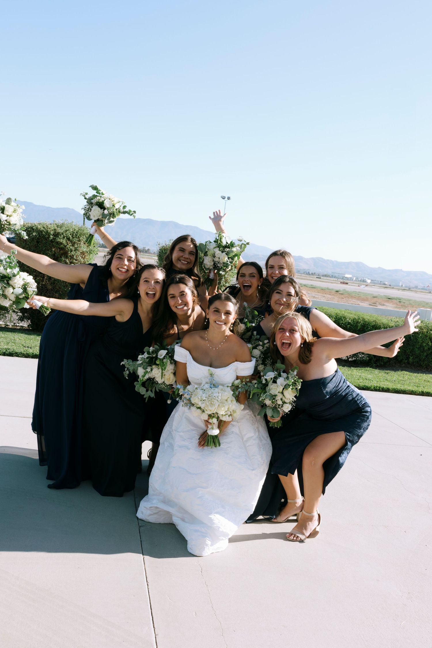 Joyful wedding party poses playfully outdoors with mountains in background.