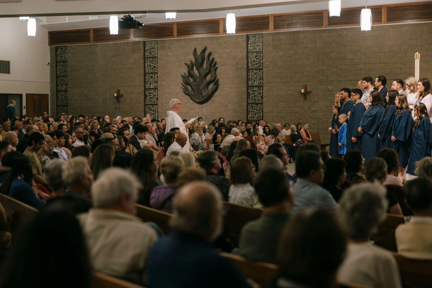 Choir in blue robes processing through a packed church congregation during a religious service.