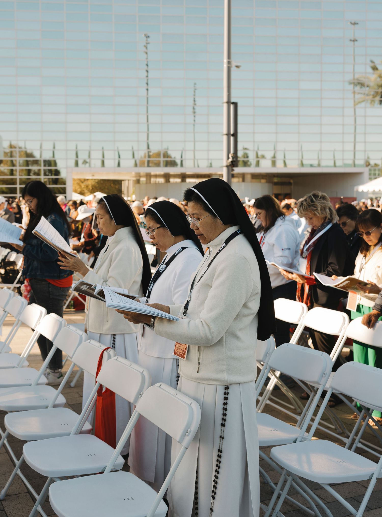 People in white attire seated in rows of folding chairs at an outdoor religious gathering.