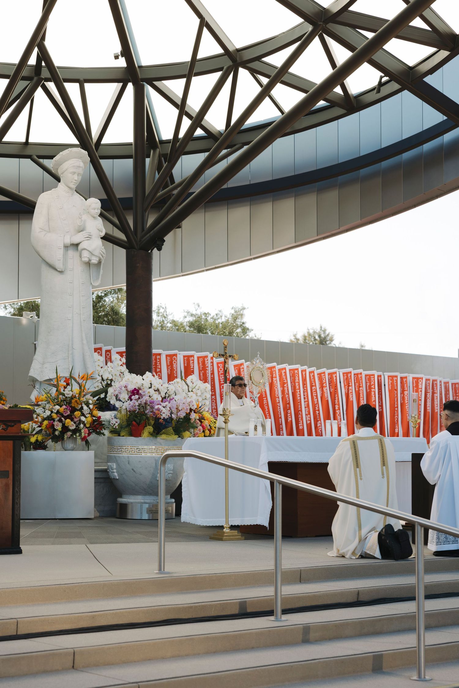 Modern covered pavilion decorated for Catholic ceremony with red banners and white altar cloths.