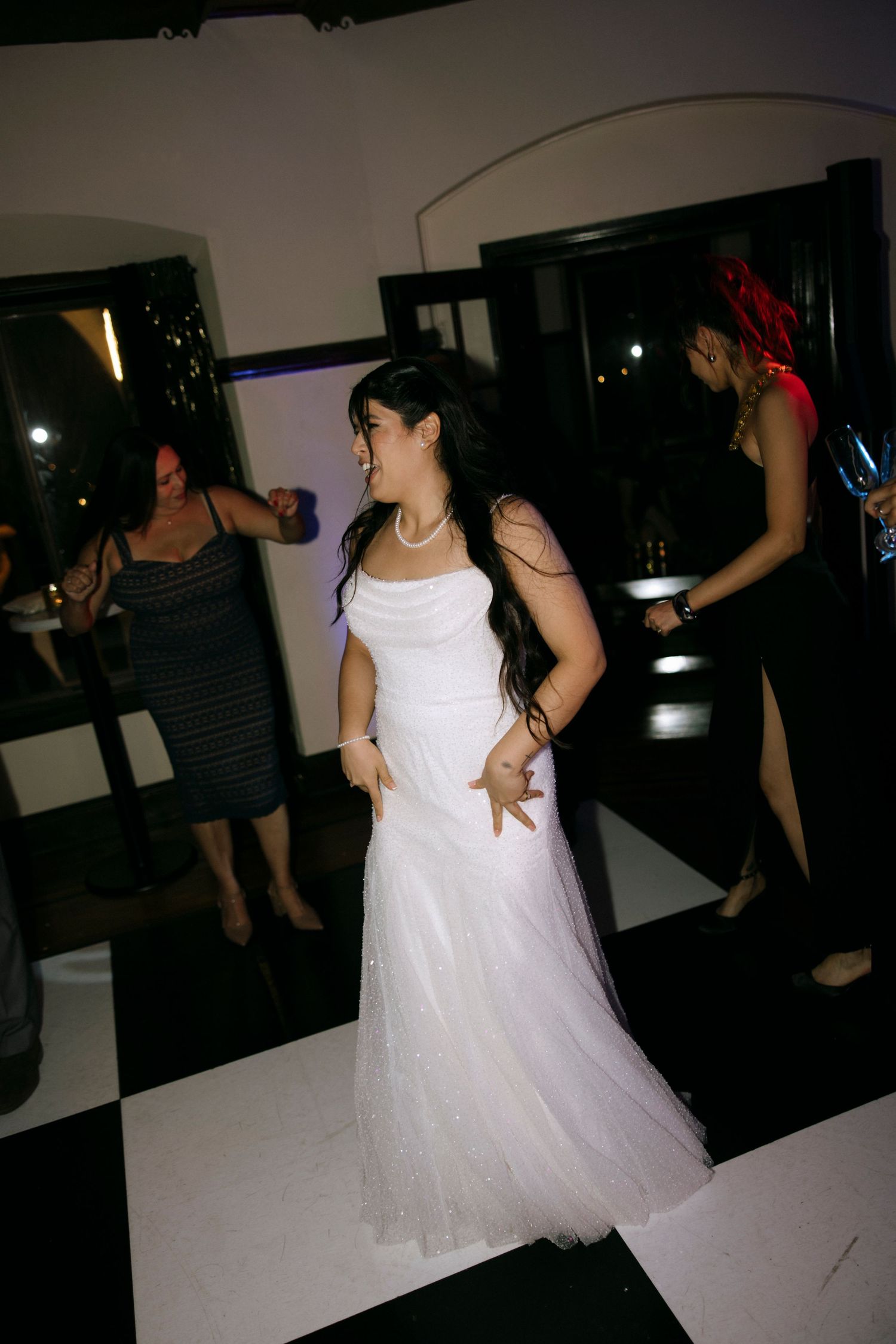 A bride in a white gown dancing at her wedding reception on a checkered dance floor.