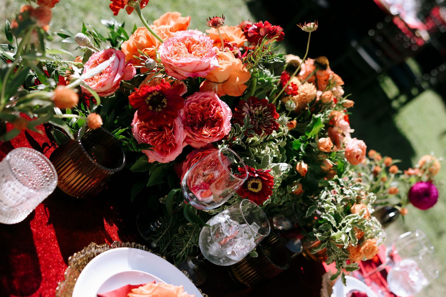 Wedding reception table decorated with vibrant coral and pink flower arrangements in vintage white vases.