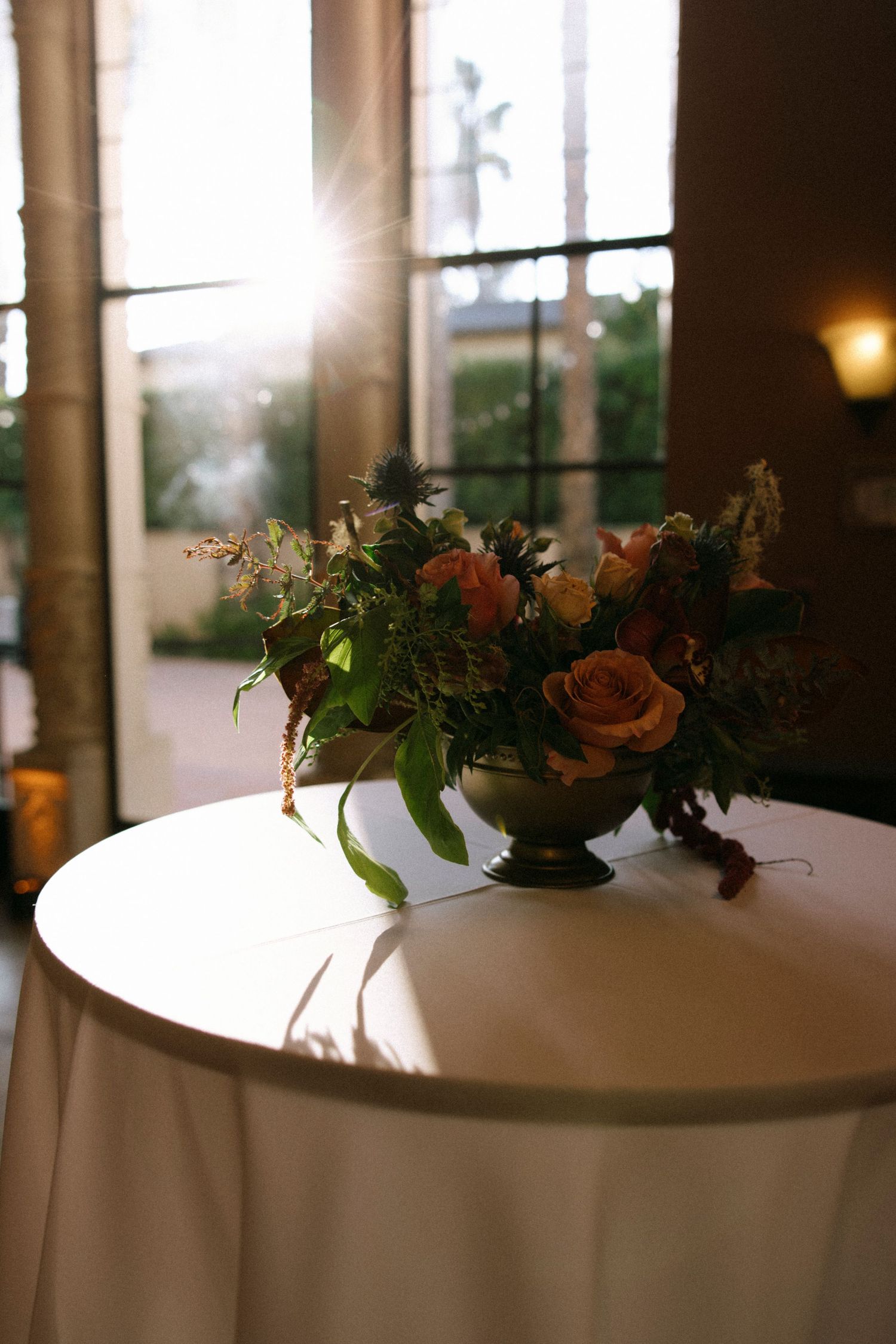 Round tables with white linens and floral centerpieces near sunlit windows.