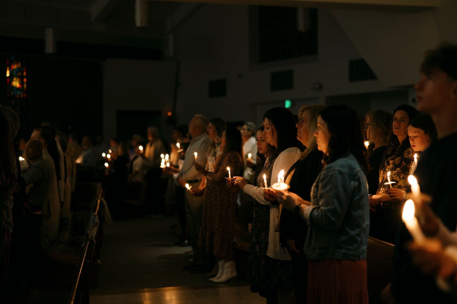 Group of people holding lit candles in a dimly lit church during a candlelight vigil ceremony.