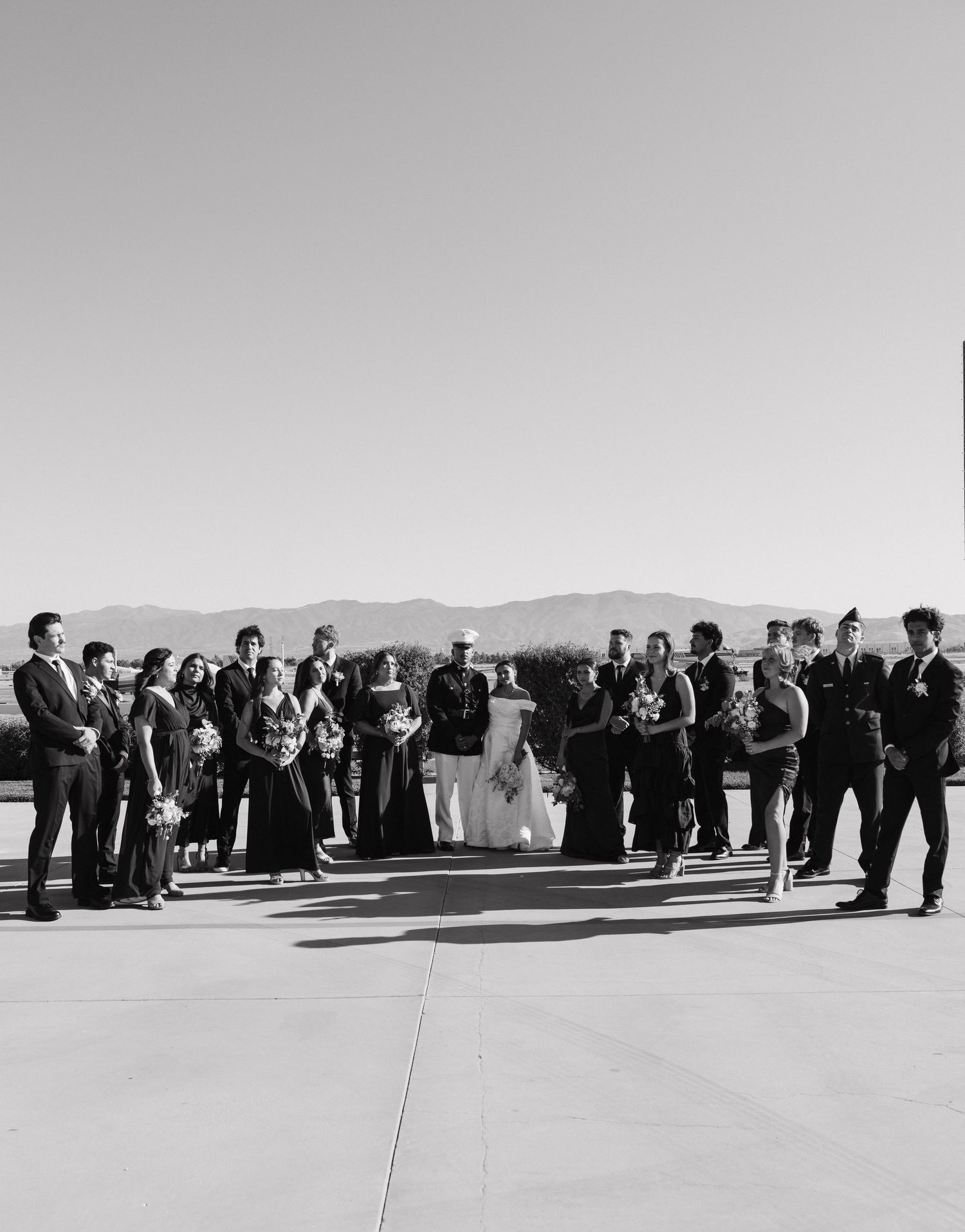 Black and white panoramic of wedding guests gathered outdoors with mountain landscape.
