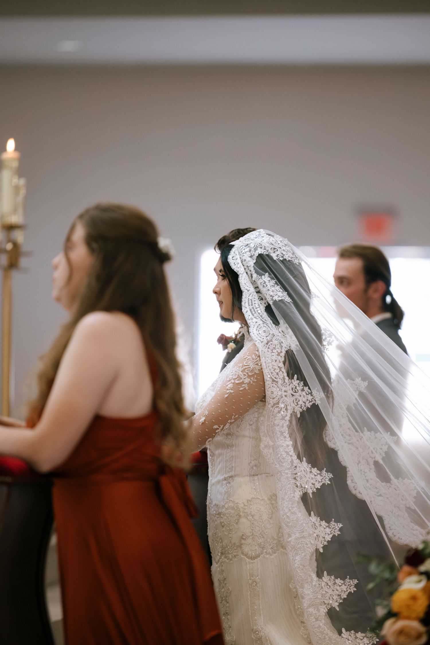 Wedding ceremony details showing bridesmaids in burgundy dresses and a flowing lace veil.