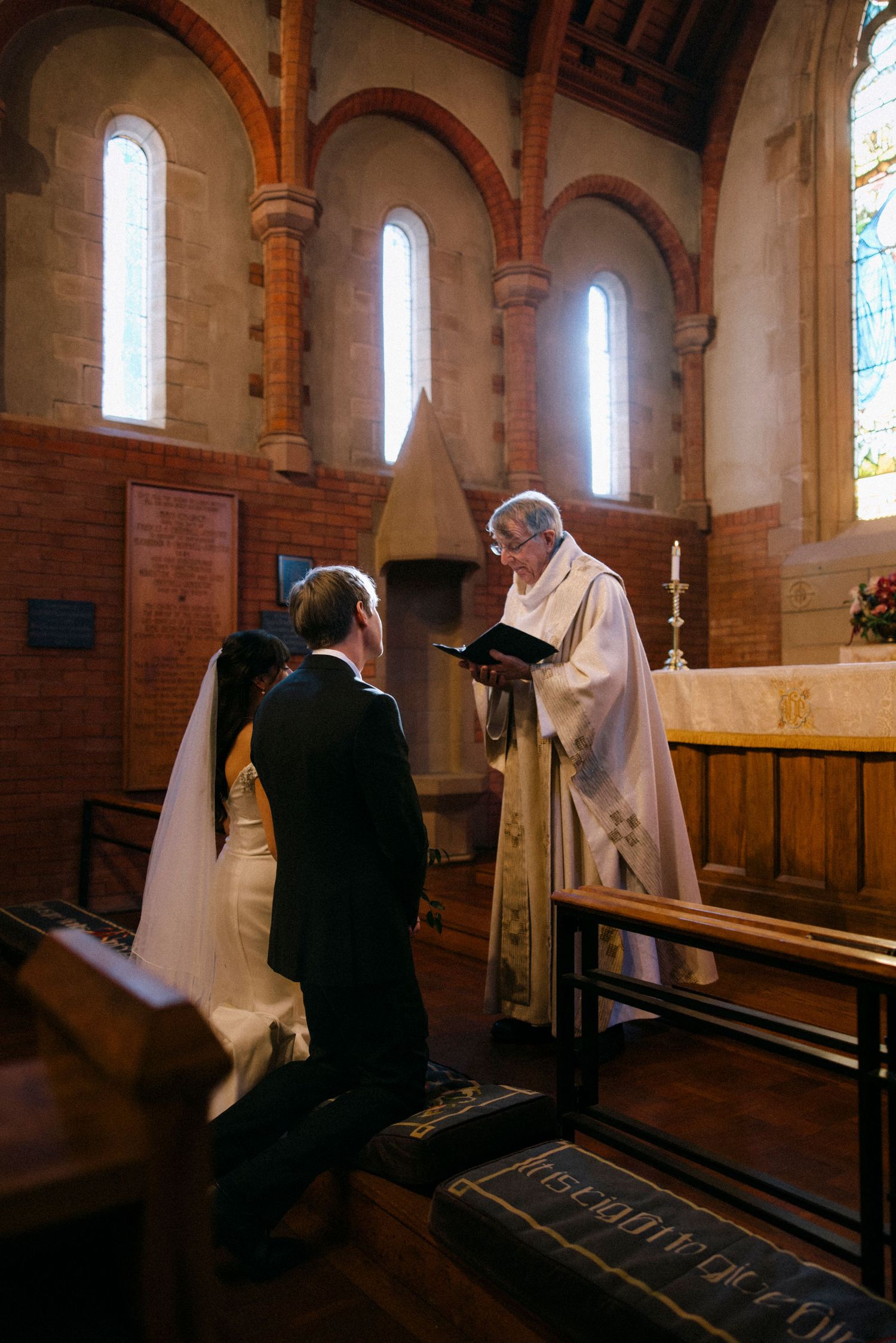 Couple kneeling at church altar with priest during traditional wedding ceremony.