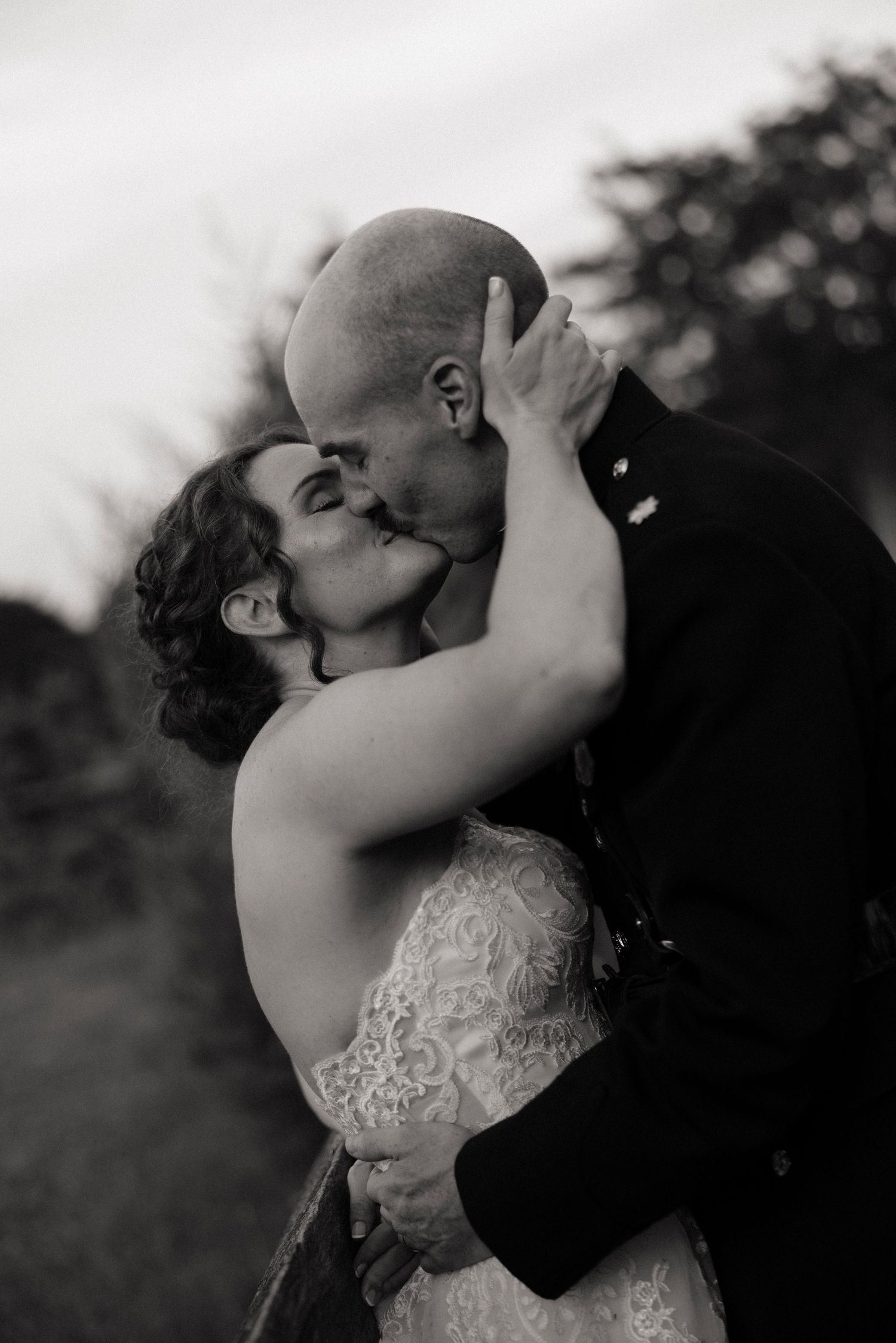 Black and white photo of a bride and groom sharing a romantic kiss outdoors on their wedding day.