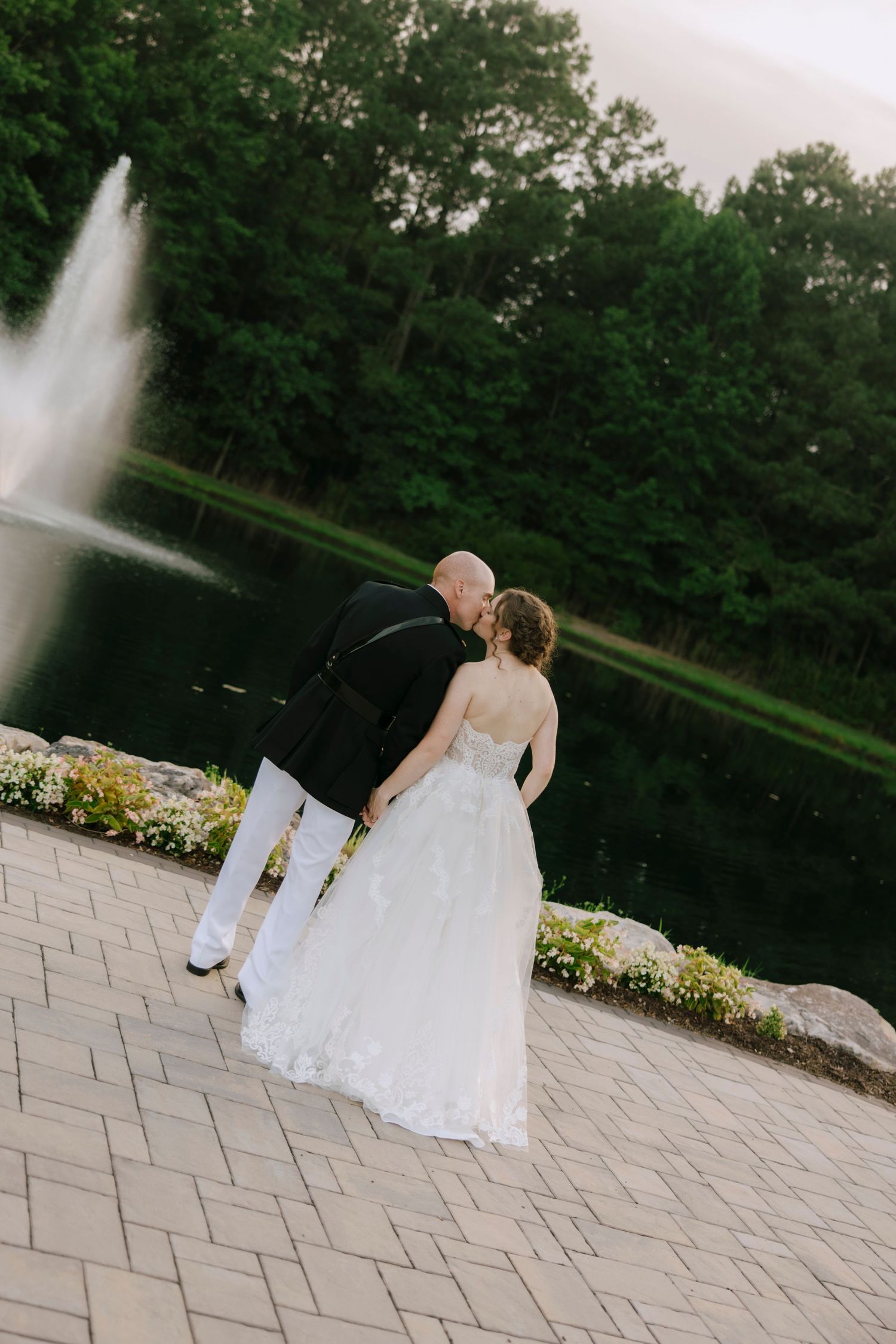 Bride and groom share a kiss near a fountain surrounded by lush greenery on their wedding day.